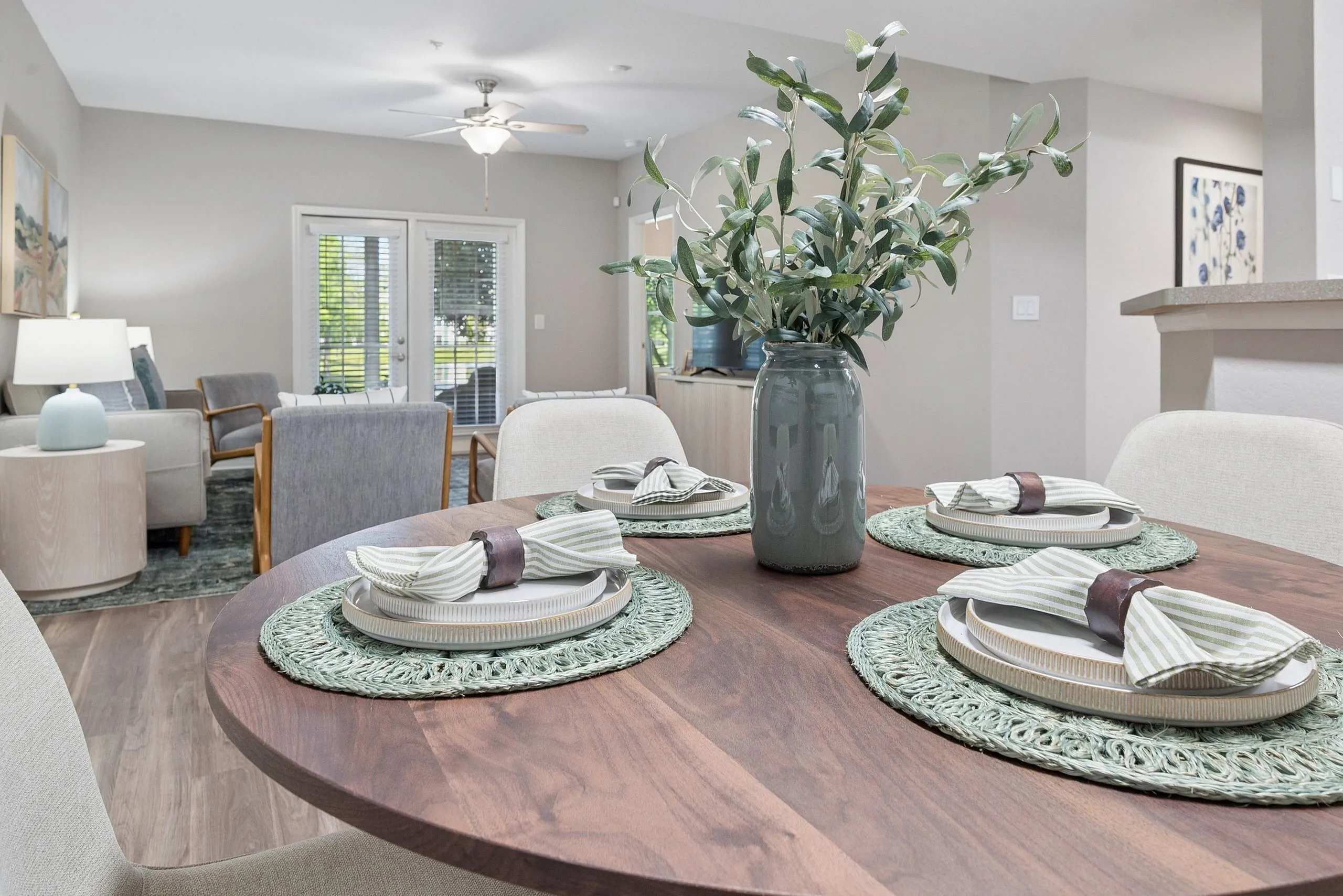 Inviting open-plan living and dining area with elegant wooden dining table, modern seating, and vibrant greenery centerpiece overlooking a serene outdoor view.