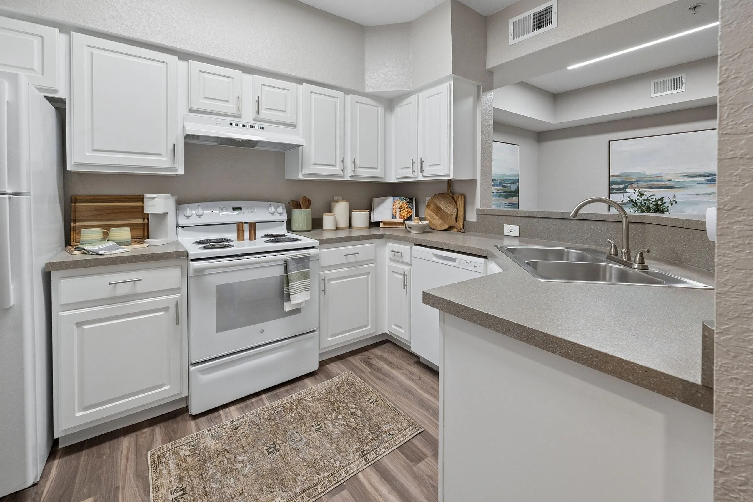 Chic modern kitchen with sleek white cabinetry, stainless steel appliances, and elegant countertops, accented by a stylish rug and open layout.