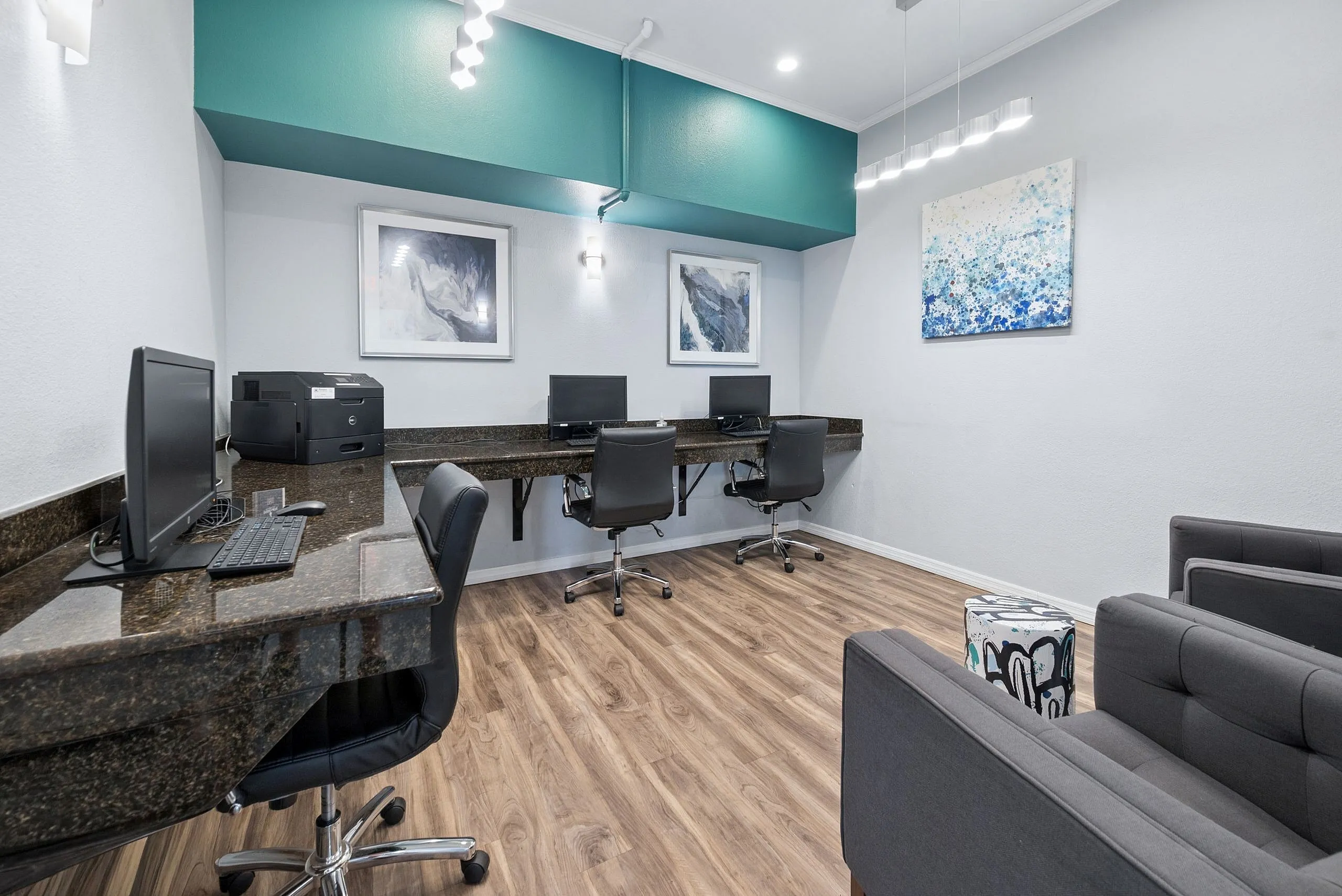 Contemporary workspace featuring sleek black desks with modern computers, plush office chairs, vibrant artwork, and elegant lighting fixtures on wood flooring.