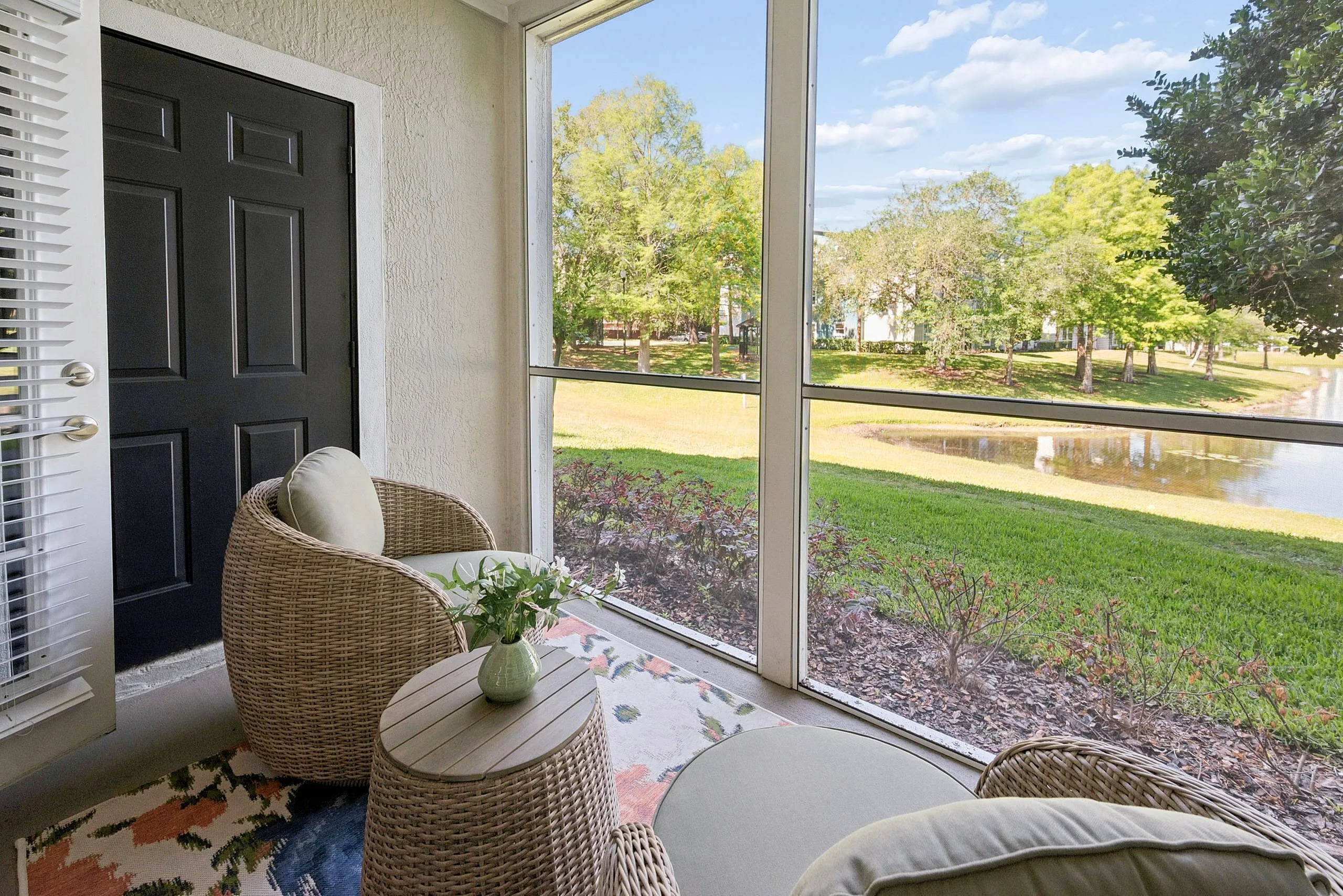 Charming patio space with cozy wicker chairs overlooking a serene pond and lush greenery, perfect for relaxation.