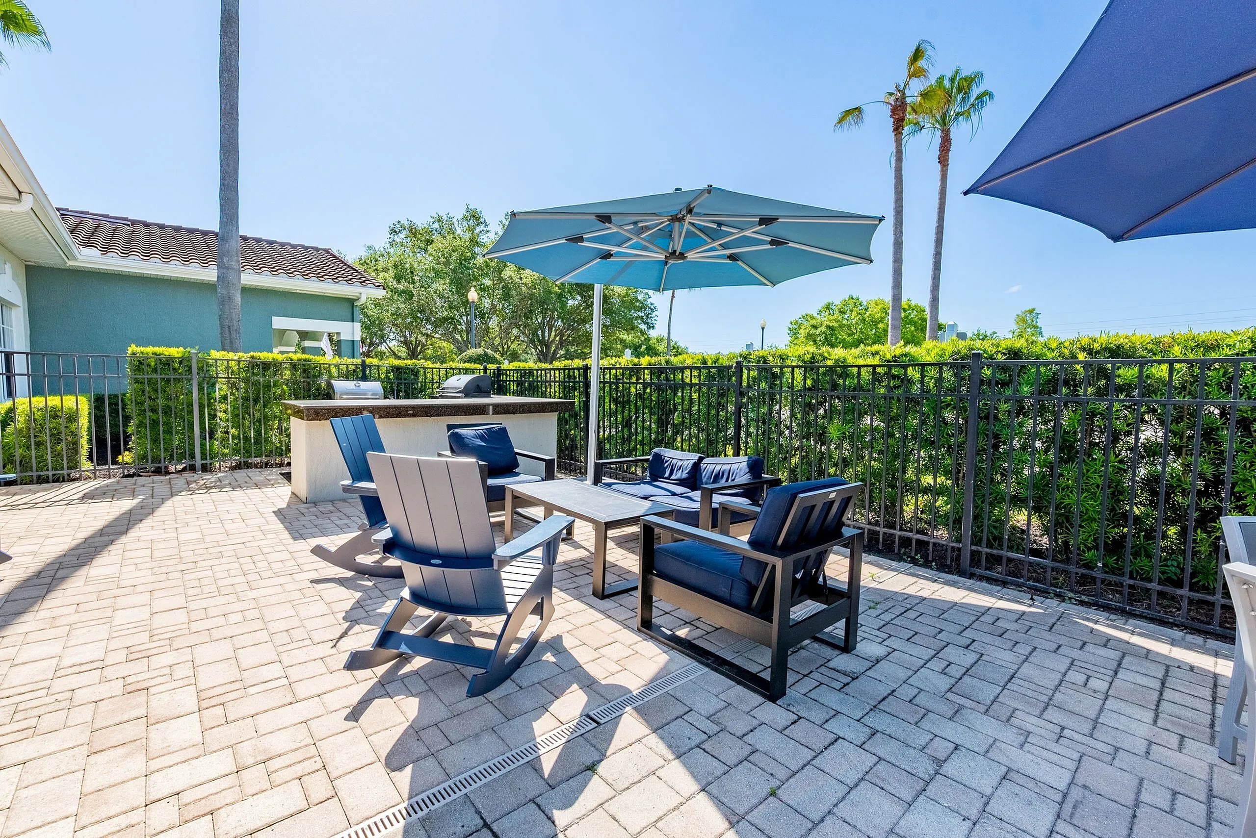 Charming outdoor patio with modern seating, vibrant umbrellas, and a built-in grill set against a lush garden backdrop.