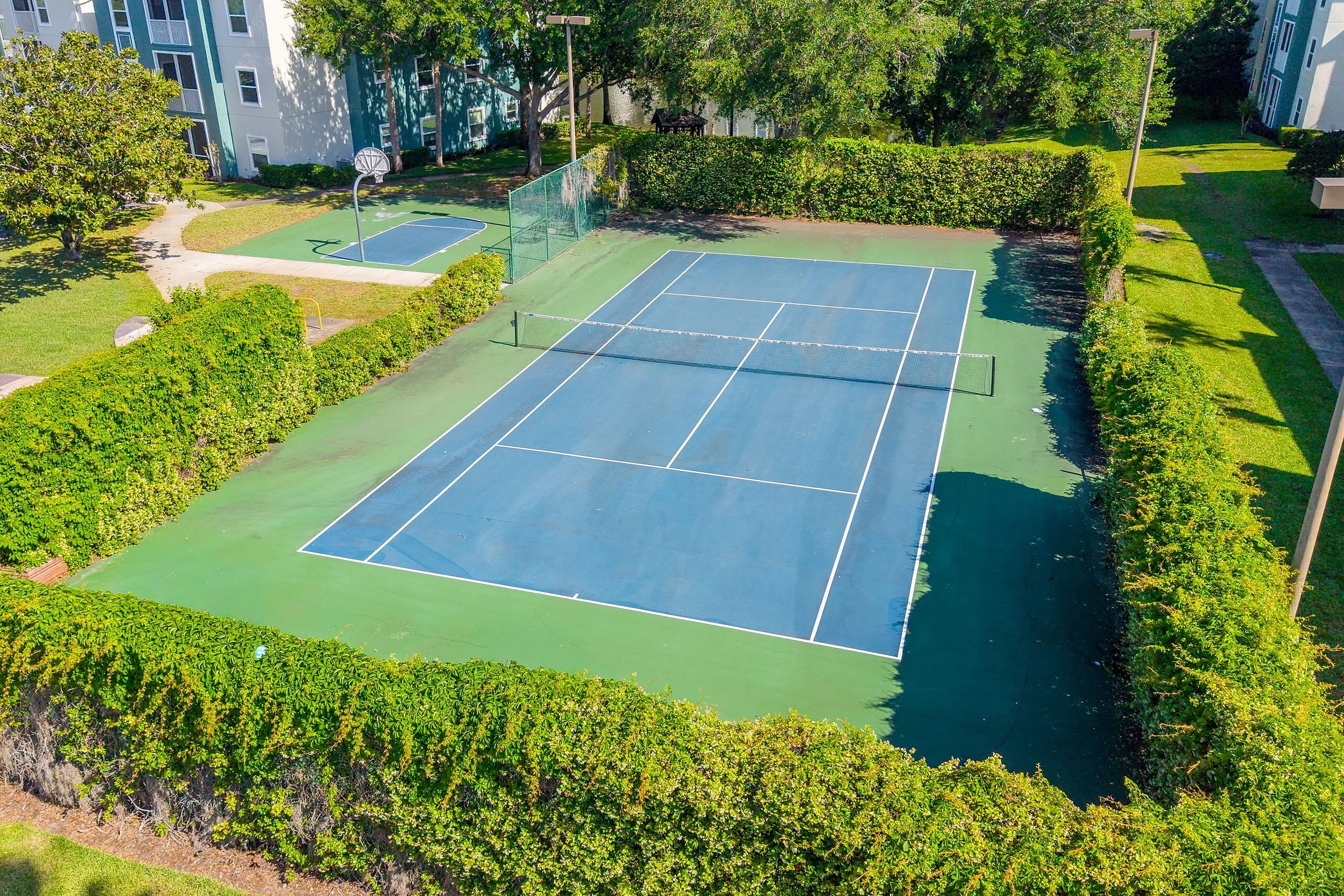 Lush community tennis court surrounded by greenery, ideal for recreation and fitness in a serene residential area.