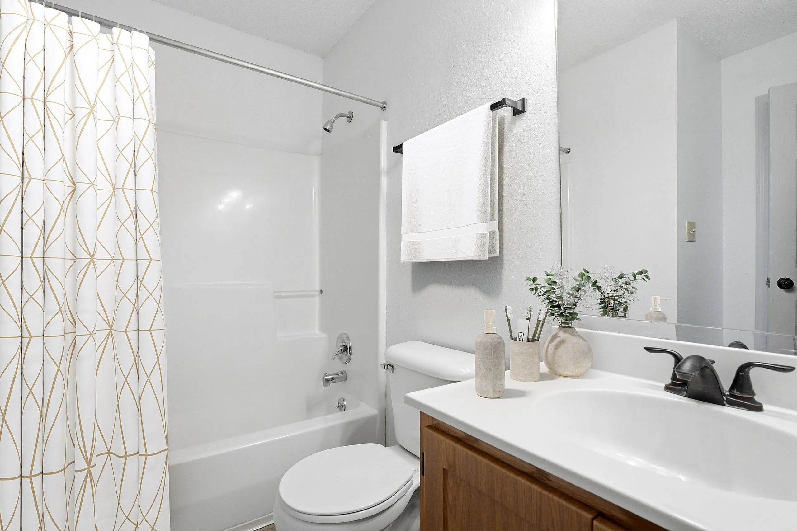 Bright and modern bathroom featuring a sleek white vanity, elegant faucet, and stylish patterned shower curtain.