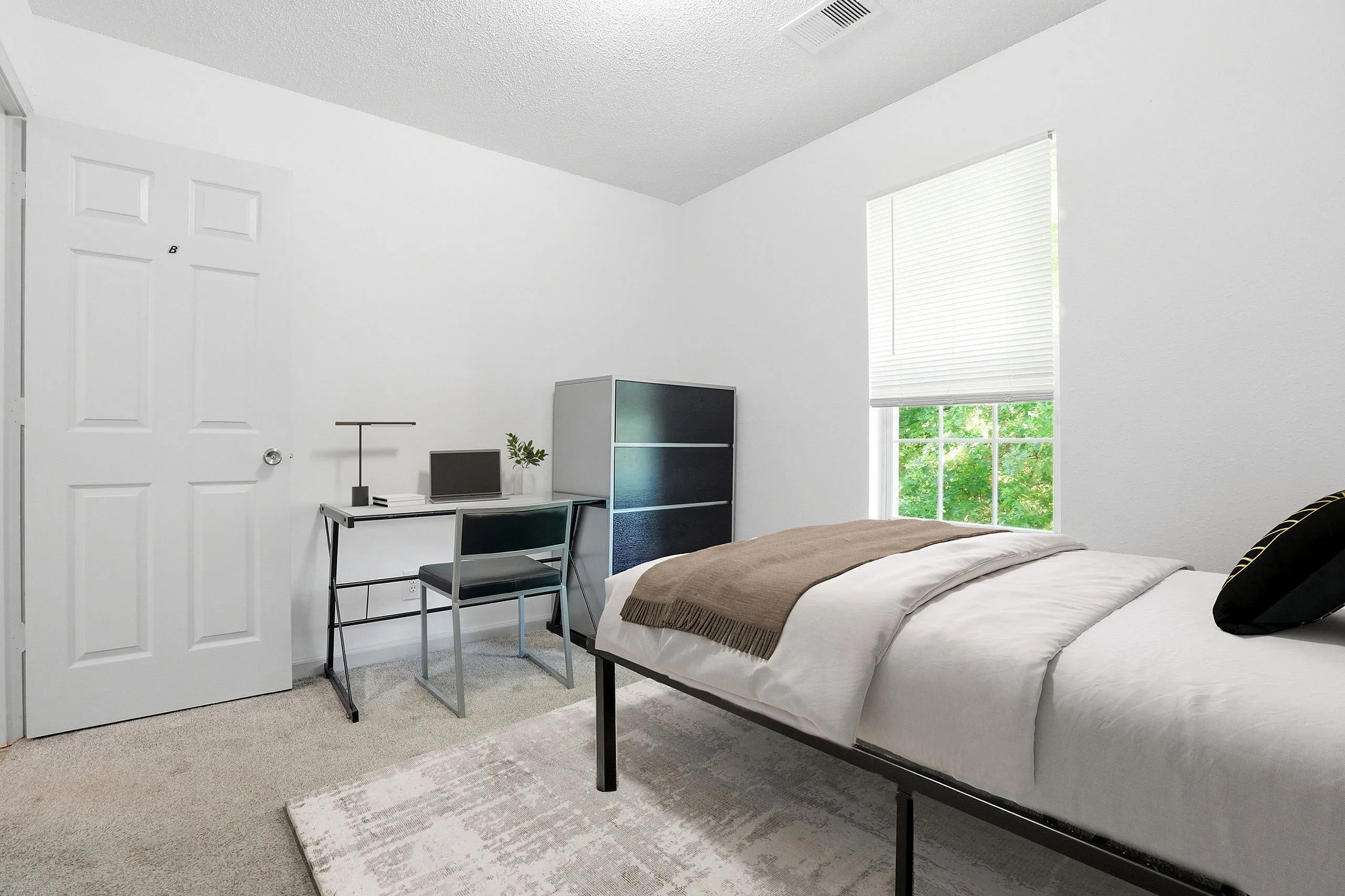 Inviting bedroom with a cozy twin bed, modern desk complete with a laptop, and ample natural light streaming through a large window.