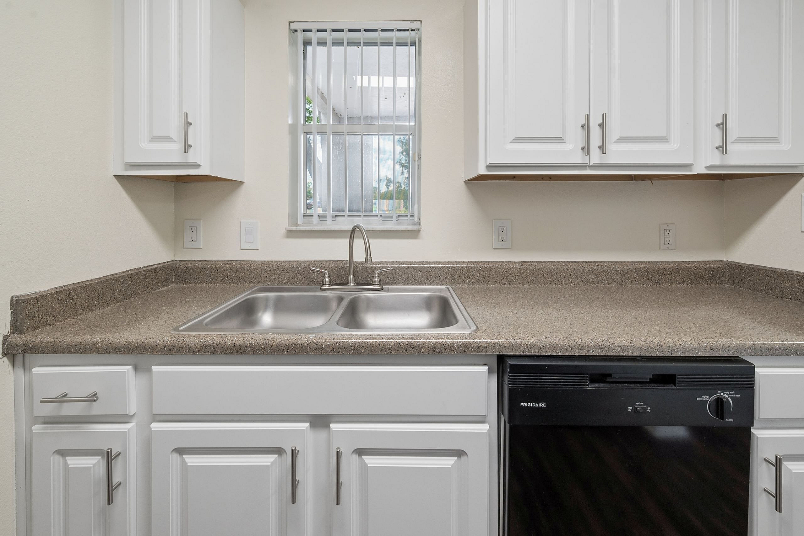 Bright kitchen with sleek white cabinets, modern countertop space, and a large window offering natural light.