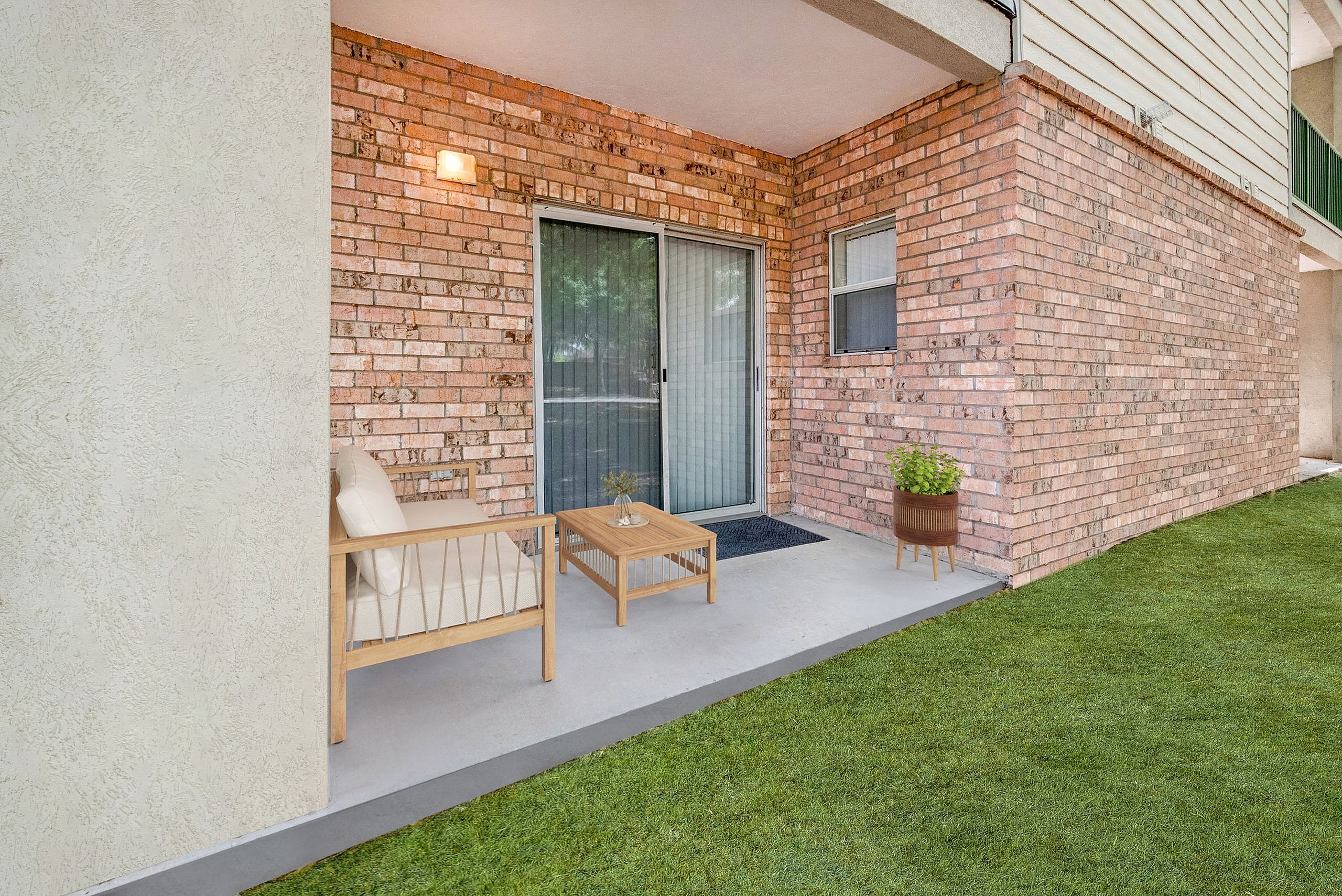 Charming outdoor patio with cozy seating, brick wall backdrop, and lush green lawn, perfect for relaxation and entertaining.