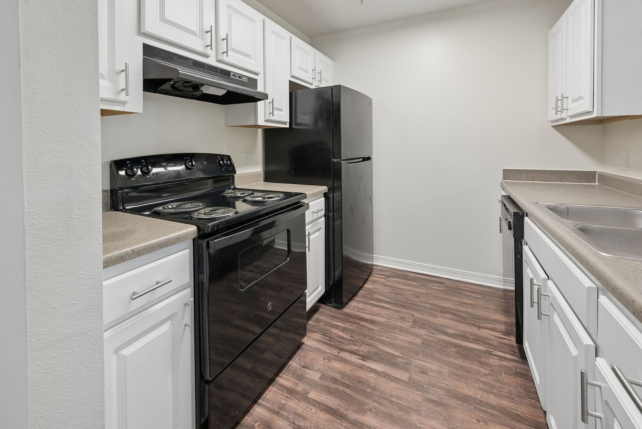 Modern kitchen with sleek black appliances, white cabinetry, and wood-style flooring, offering a chic culinary space.