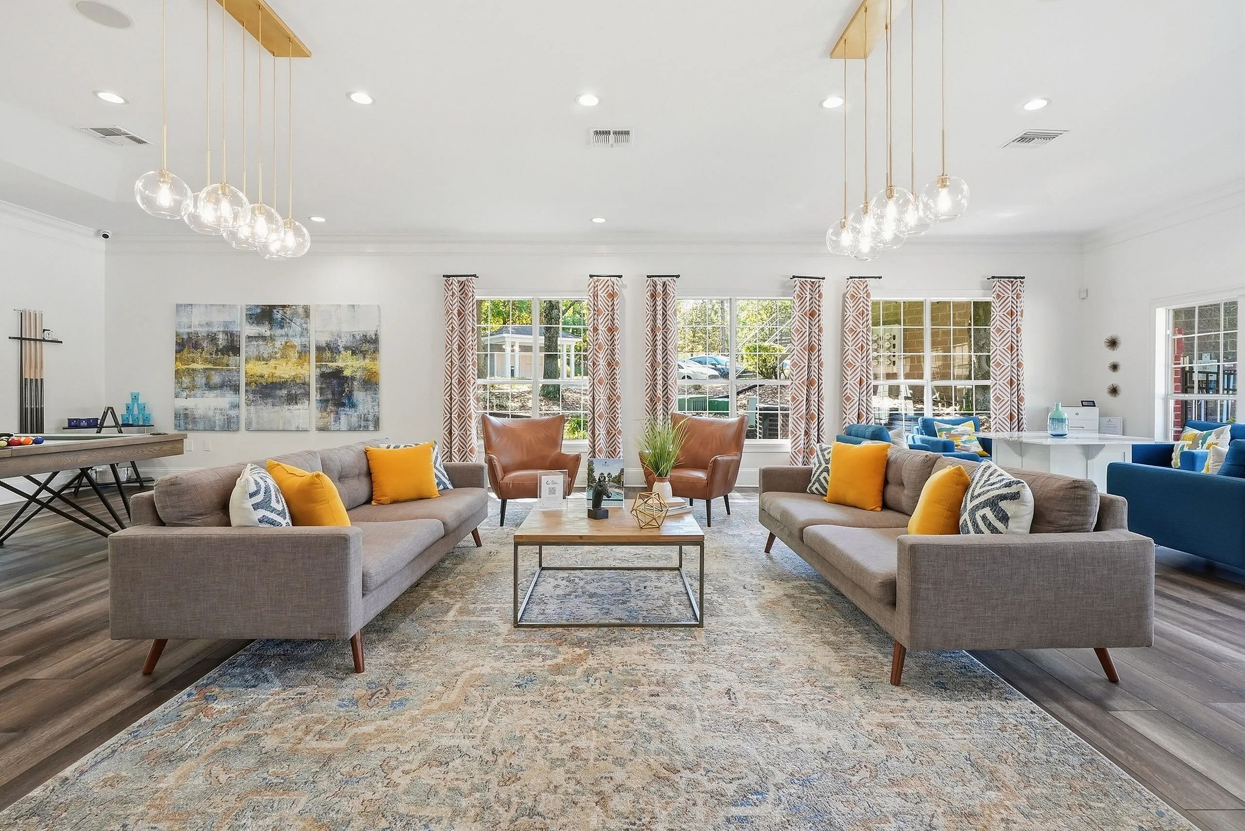 Elegant living room with modern decor, featuring chic sofas, vibrant pillows, and large windows with patterned curtains flooding the space with natural light. A pool table and stylish seating make it perfect for entertaining.