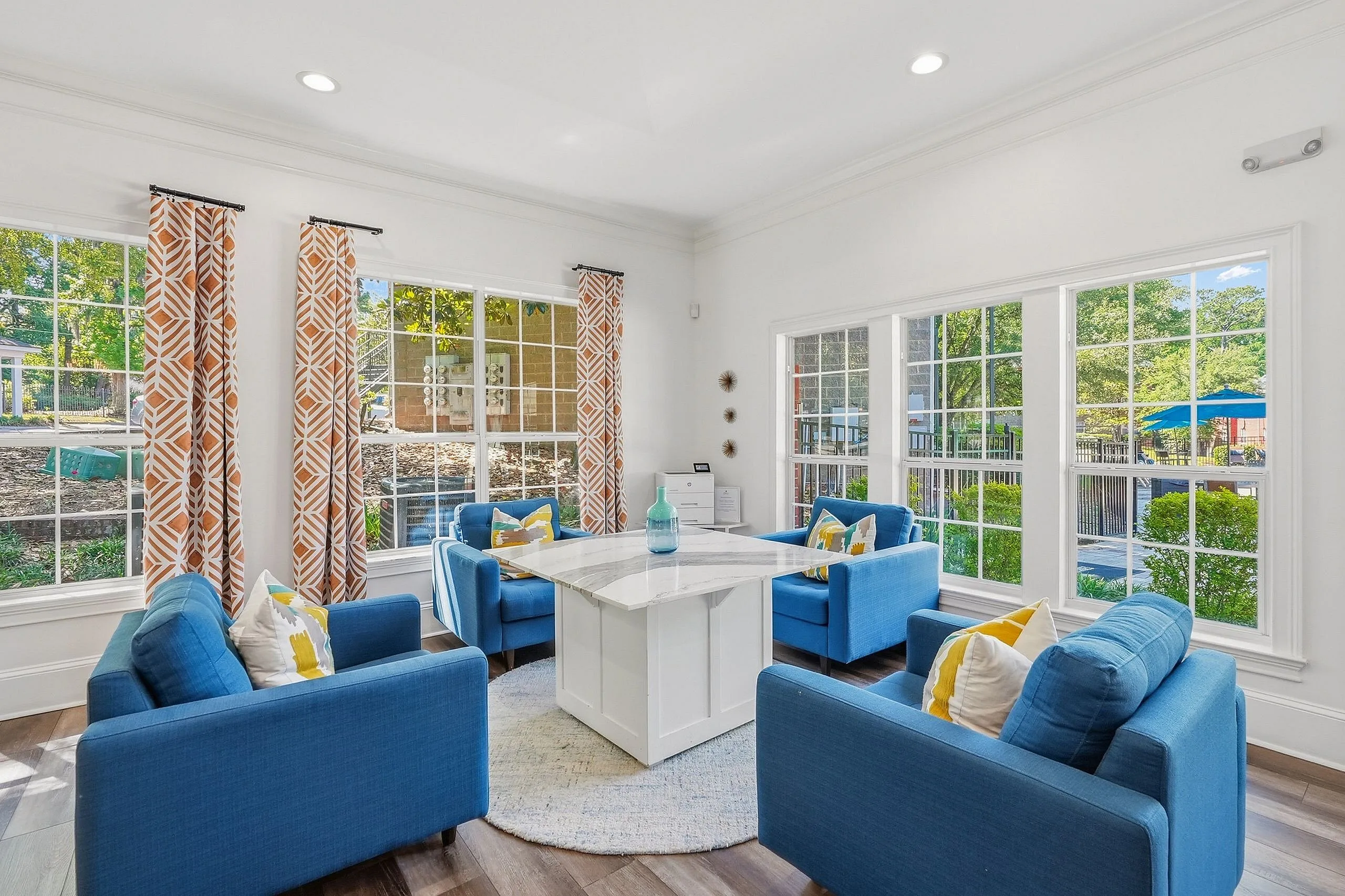 Bright and inviting living space with large windows, vibrant blue seating, and patterned curtains overlooking a lush outdoor view.