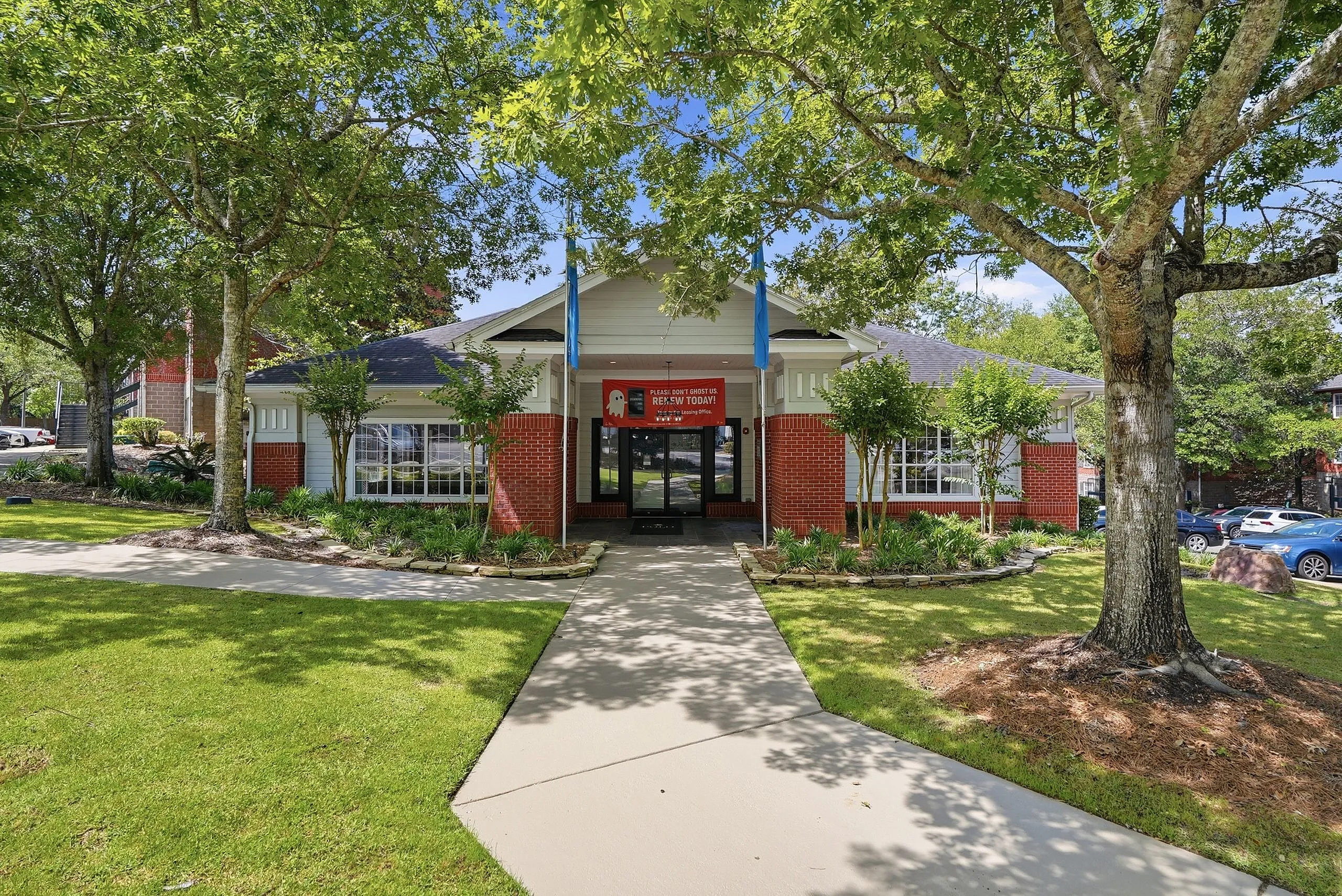Charming apartment building entrance with vibrant landscaping and lush greenery on a sunny day, featuring a welcoming path leading to stylish brick architecture.
