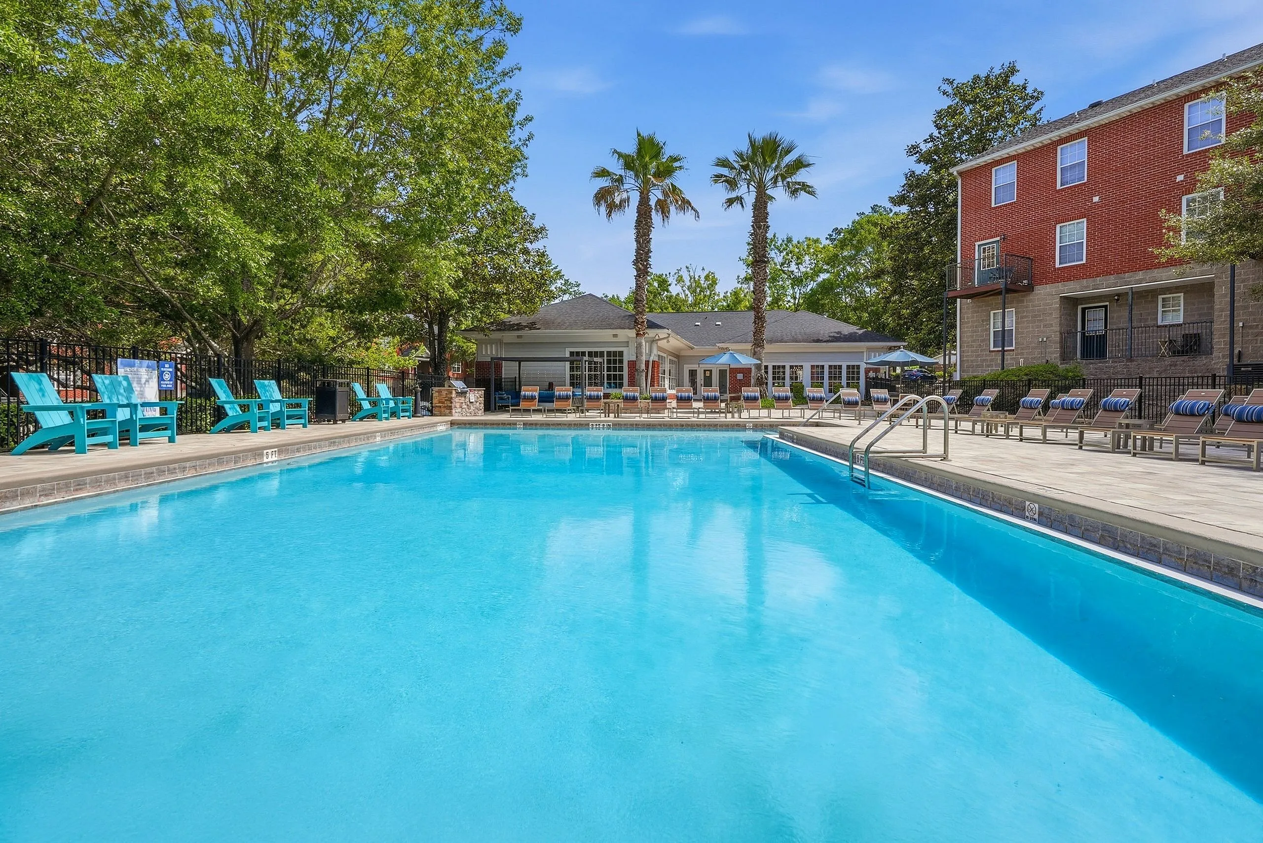 Inviting apartment community pool area with vibrant blue water, surrounded by lush greenery and comfortable seating, perfect for relaxation and socializing.