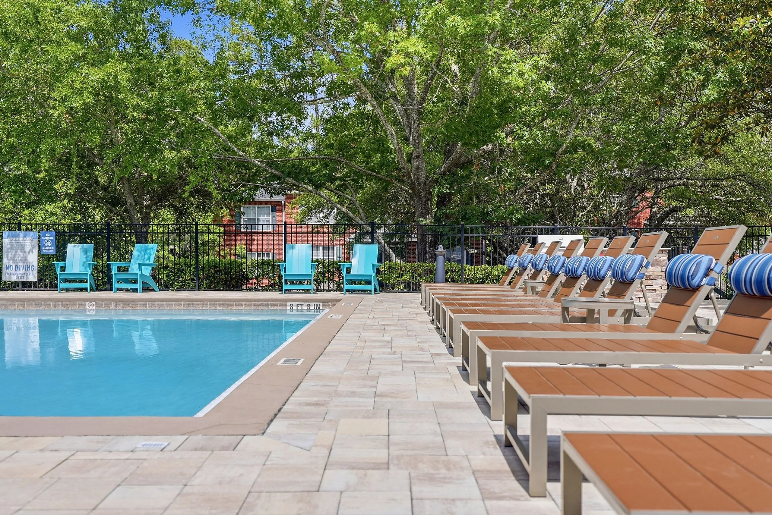 Inviting swimming pool area with stylish sun loungers and vibrant teal chairs, surrounded by lush greenery for a serene escape.