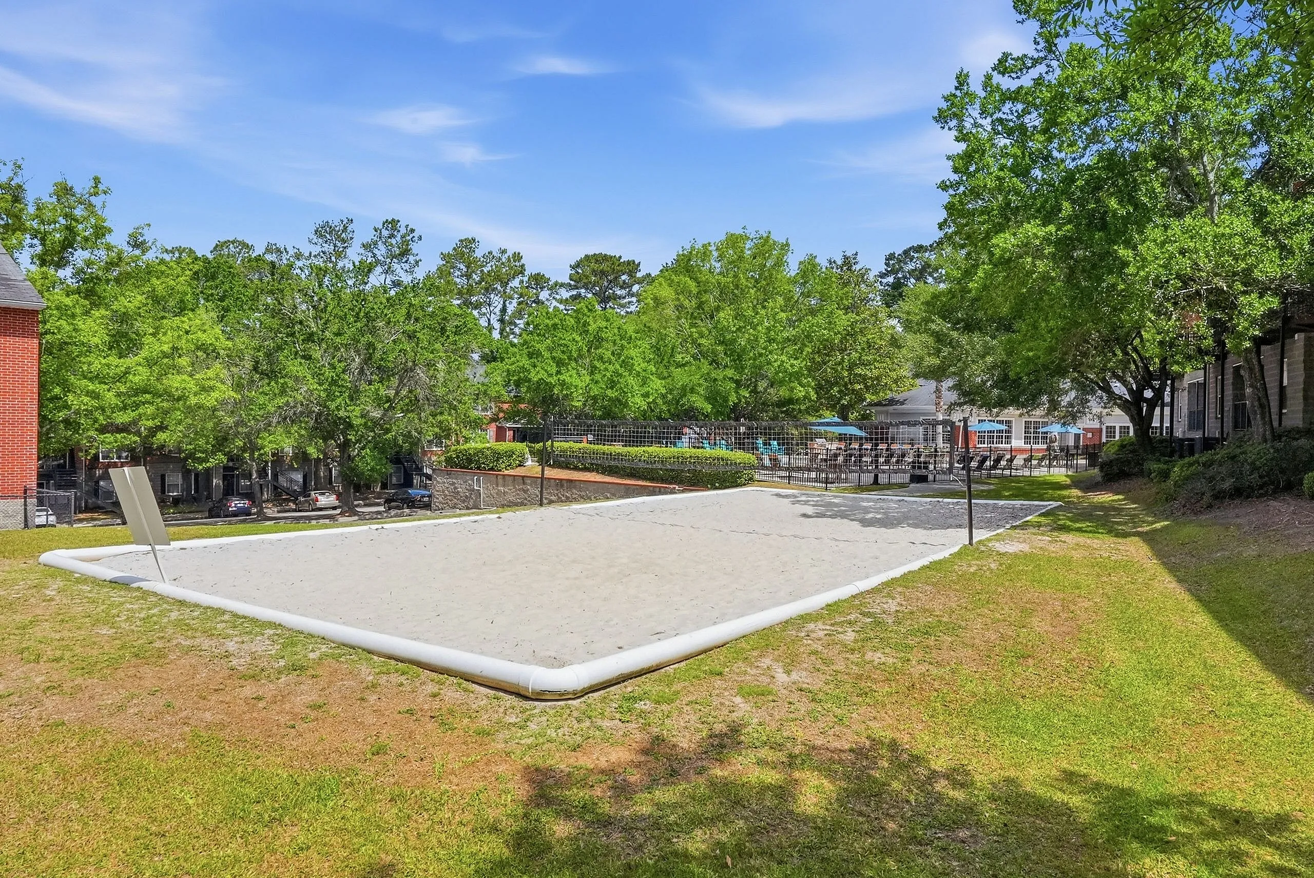 Inviting outdoor sand volleyball court surrounded by lush greenery and modern apartment amenities.