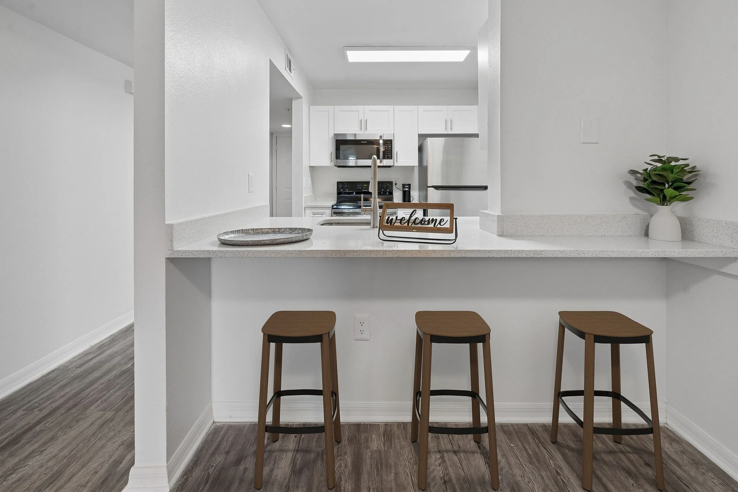 Modern kitchen with sleek granite countertops and stylish bar stools, featuring stainless steel appliances and bright white cabinetry, creating an inviting culinary space.