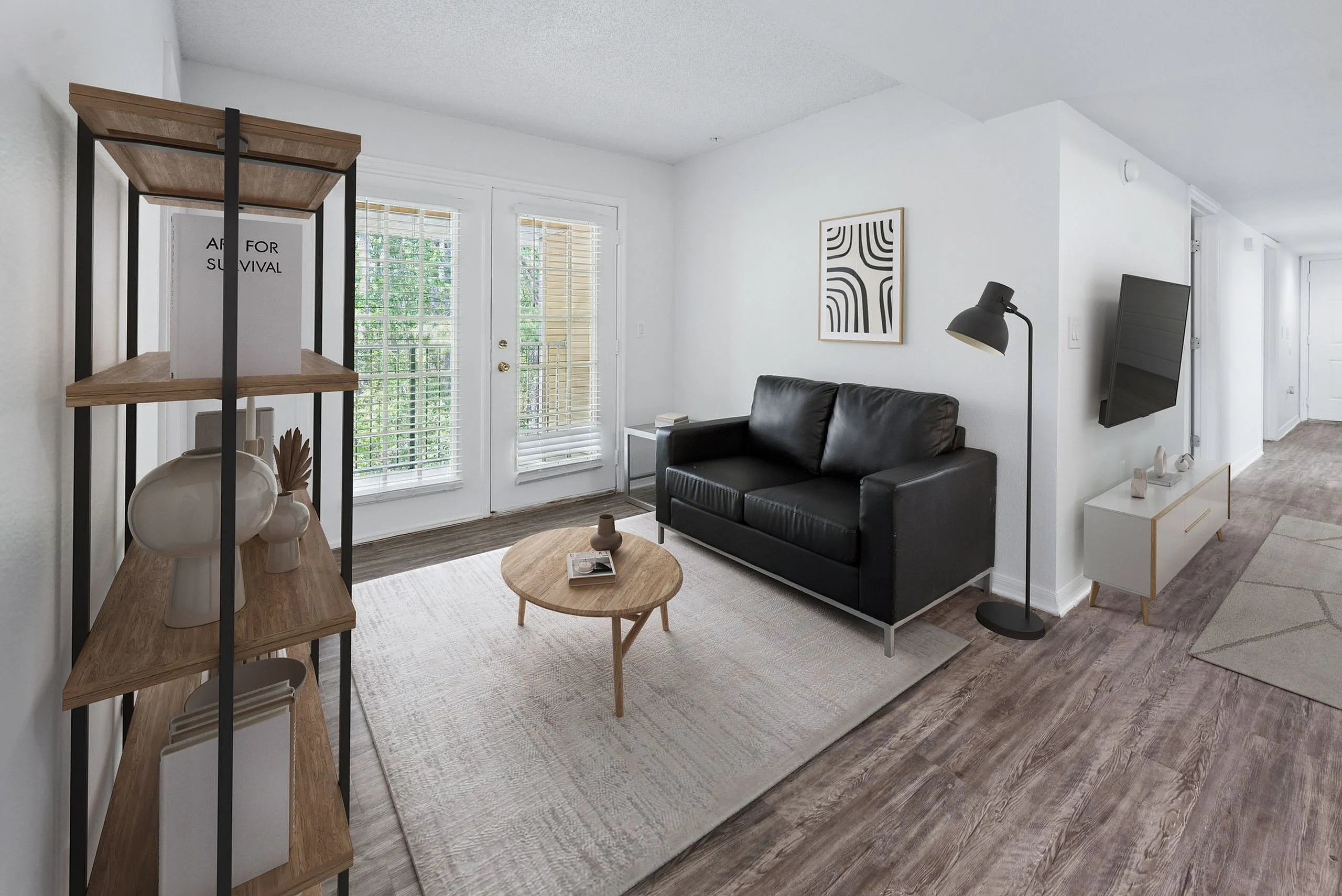 Chic living room with modern black sofa, stylish artwork, sleek floor lamp, and glass double doors opening to a lush view, highlighted by elegant wood flooring.