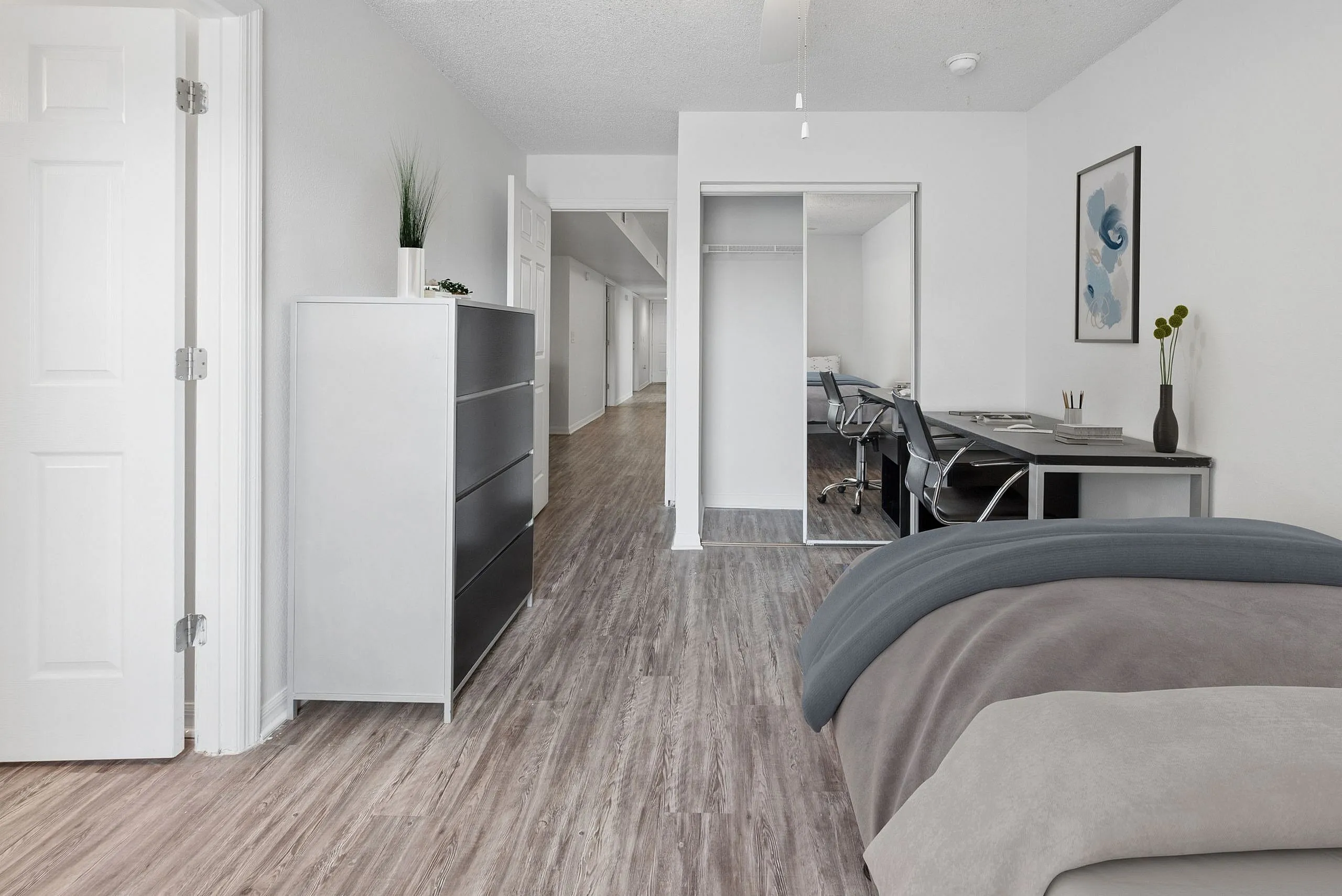 Modern bedroom with sleek wooden floors, a contemporary dresser, and a stylish workspace featuring a dual desk setup and sophisticated wall art.