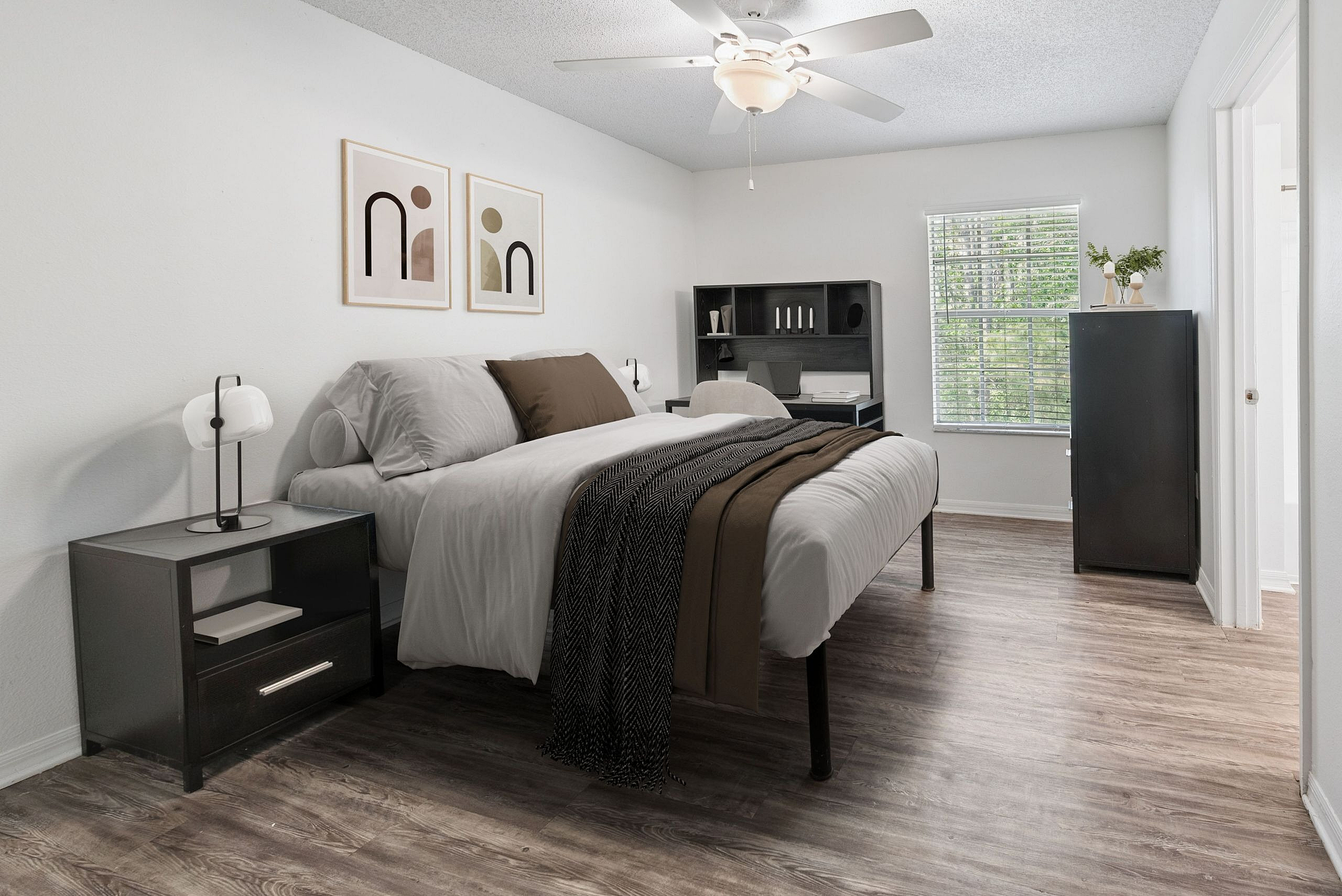 Elegant bedroom with modern decor, featuring a cozy bed, stylish artwork, and a work desk, illuminated by natural light from a large window.