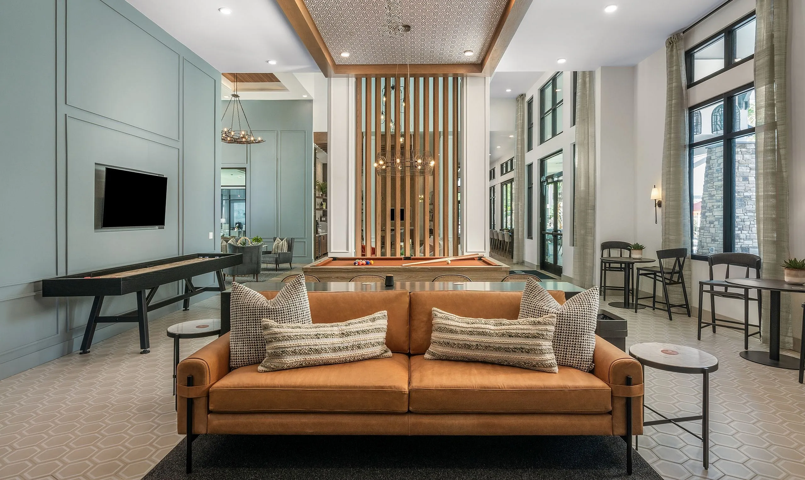 Contemporary entertainment room featuring a stylish leather sofa, elegant pool table, and modern decor with expansive windows and natural light.