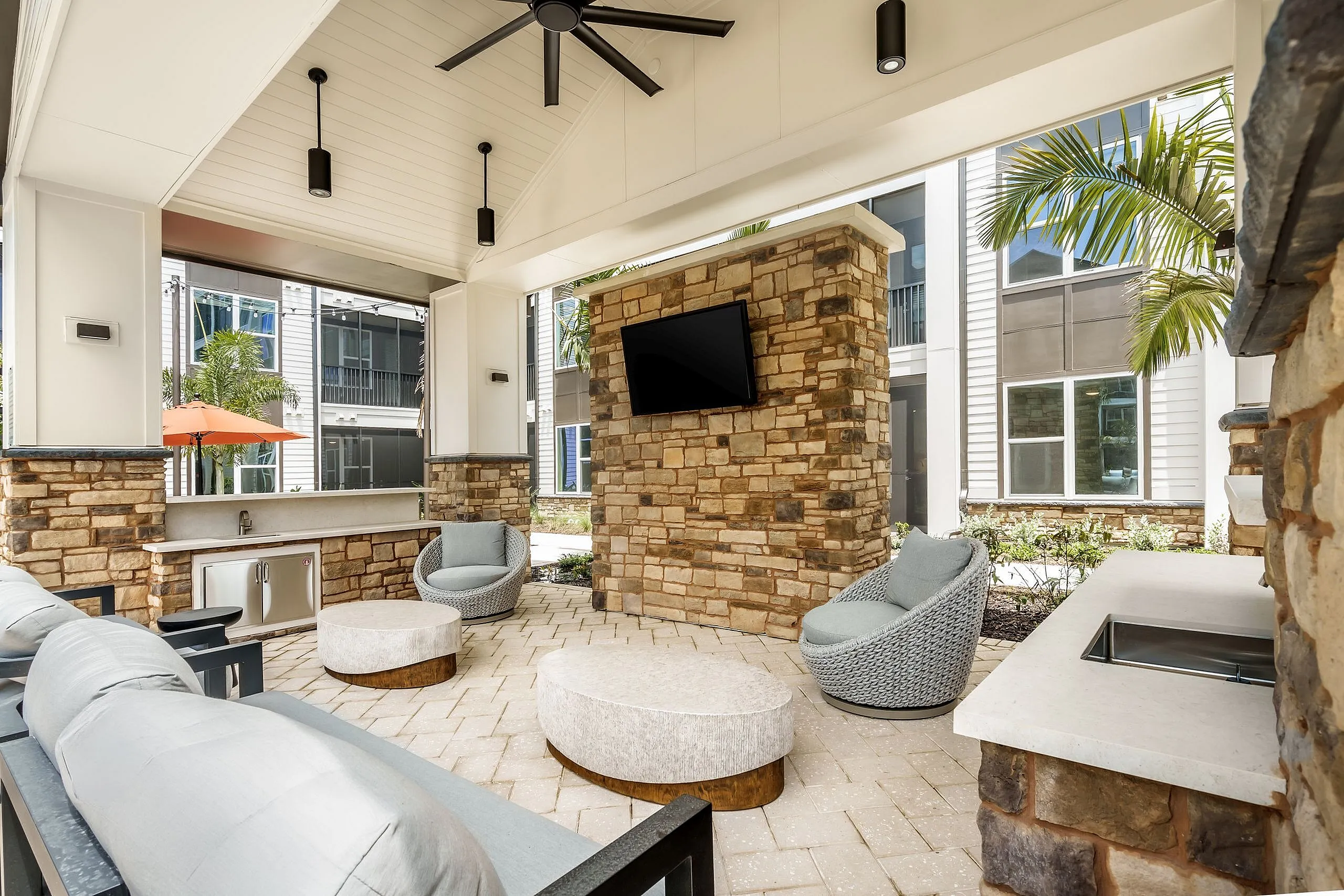 Luxurious outdoor lounge area with modern seating, stone accents, and a mounted TV, perfect for entertaining and relaxation.