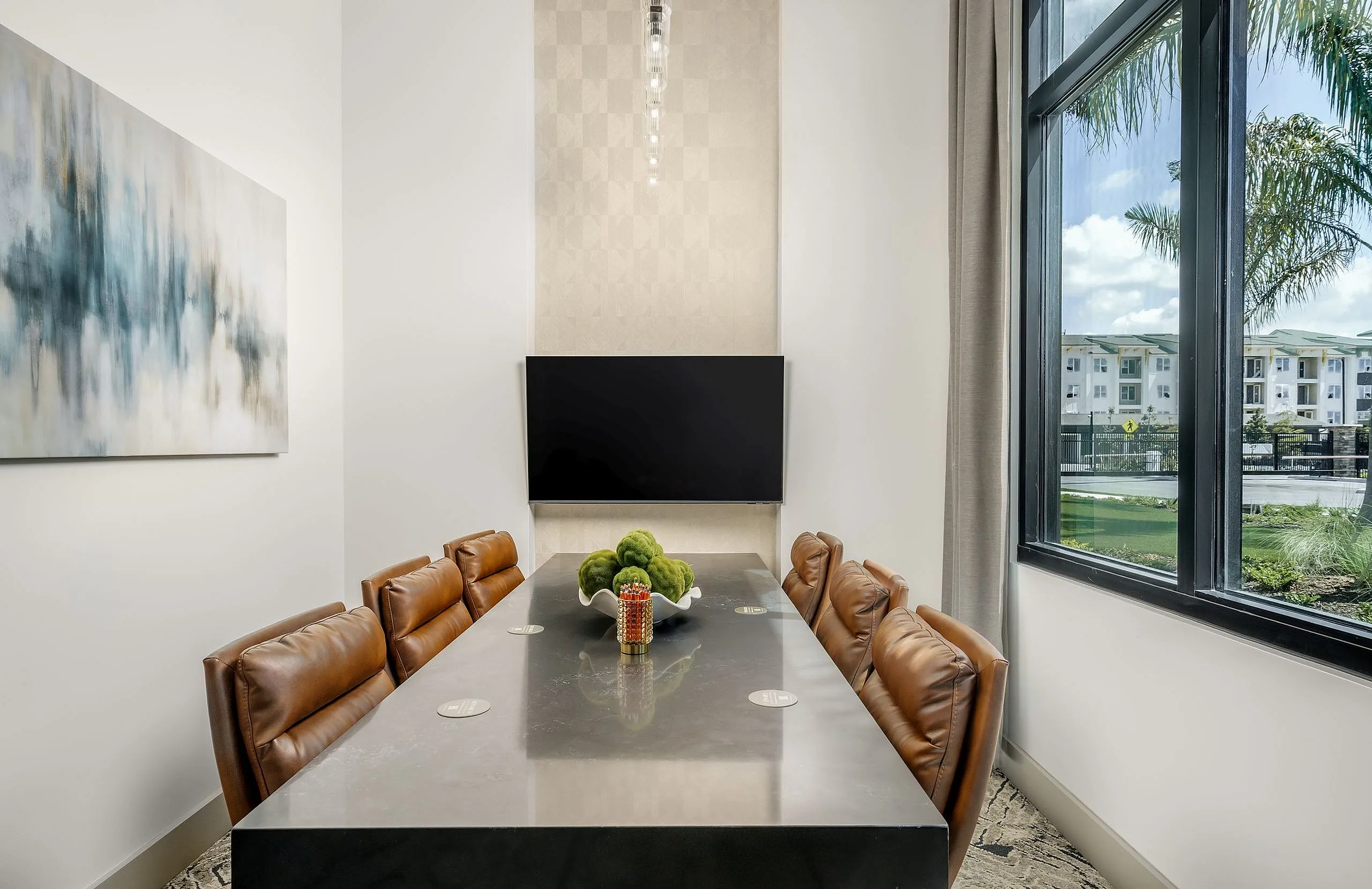 Elegant meeting room with plush leather chairs, a modern table, abstract wall art, and a large window providing a view of a serene outdoor landscape.