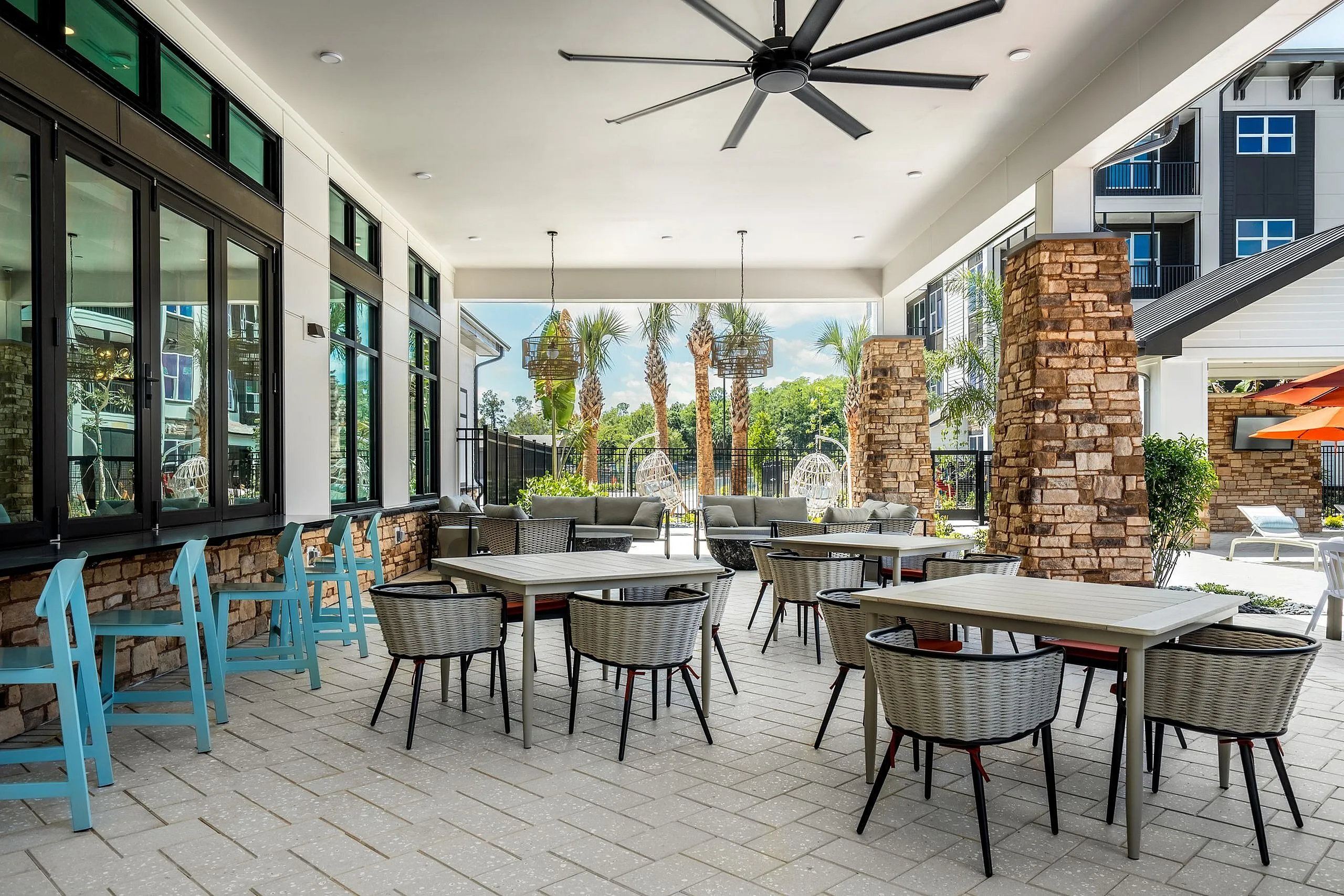 Inviting covered patio area with stone accents, stylish seating, and views of lush landscaping and palm trees.