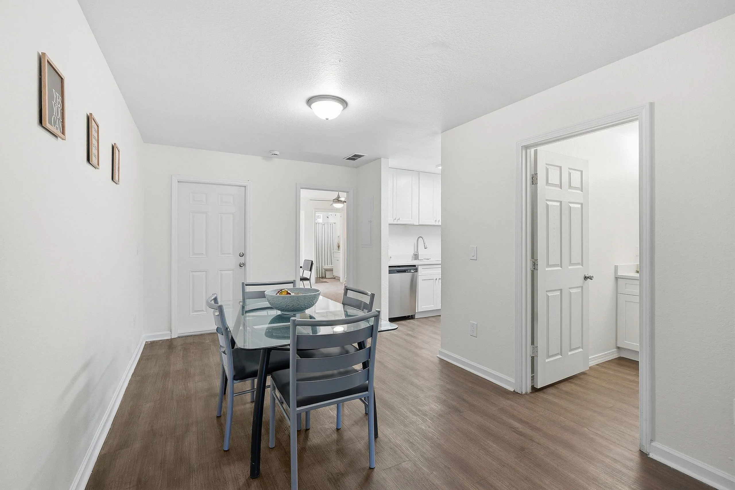 Bright and inviting dining area featuring a modern glass table, elegant light fixtures, and seamless access to a sleek kitchen and cozy living space.