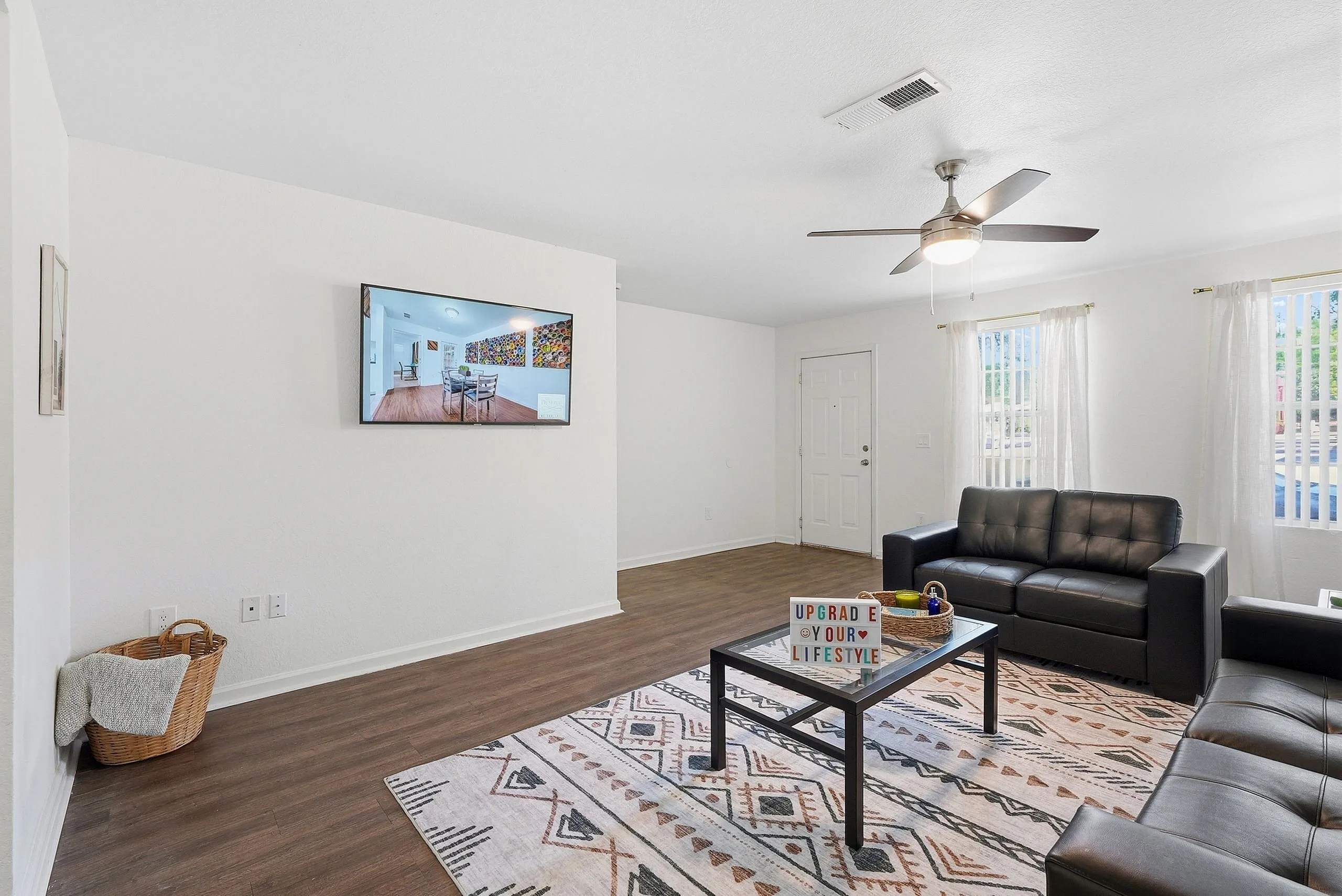 Inviting living room featuring stylish decor, a cozy black leather sofa, a modern ceiling fan, and natural light streaming through sheer curtains.