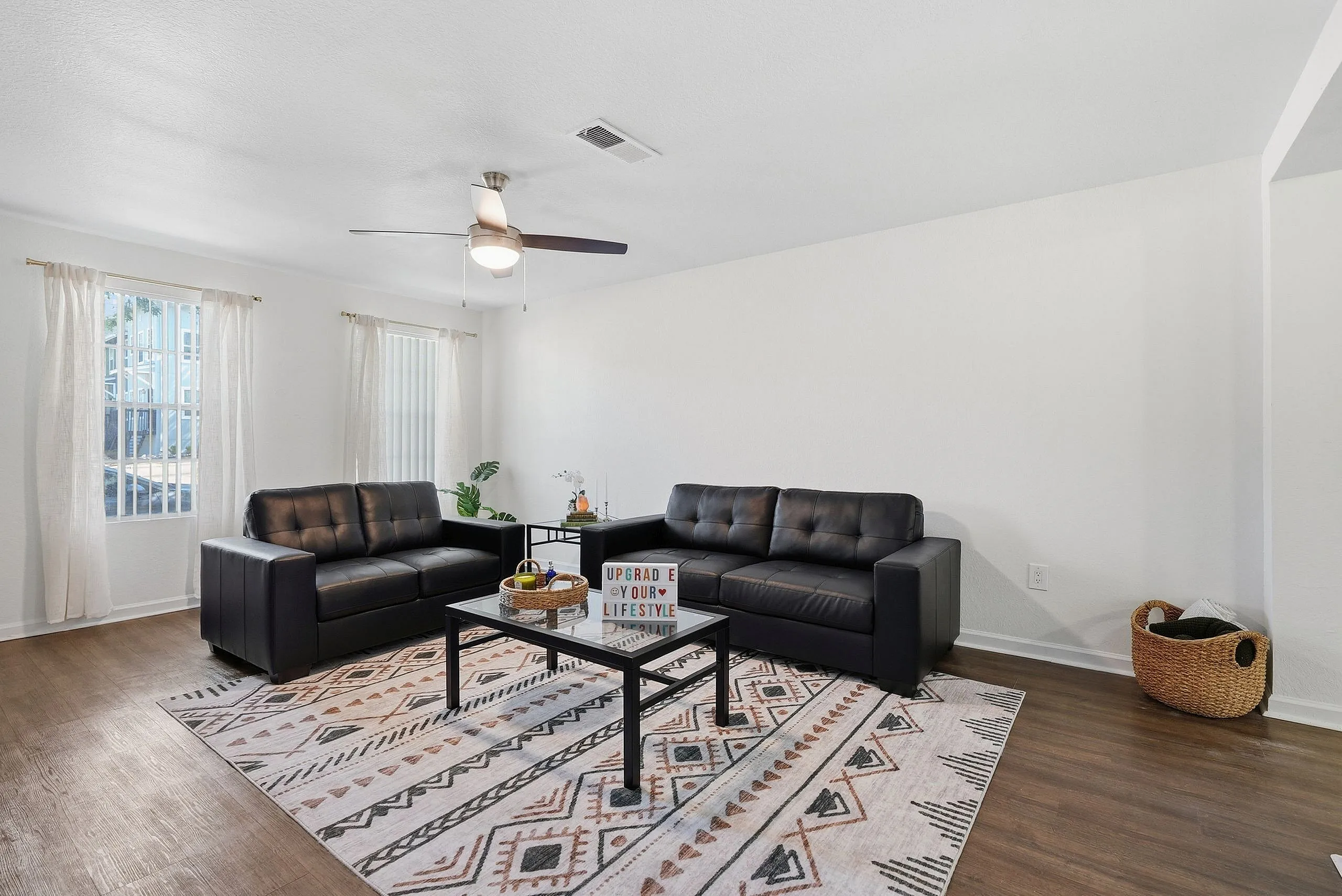 Modern living room with chic black leather sofas, a stylish geometric rug, and natural light filtering through sheer curtains.