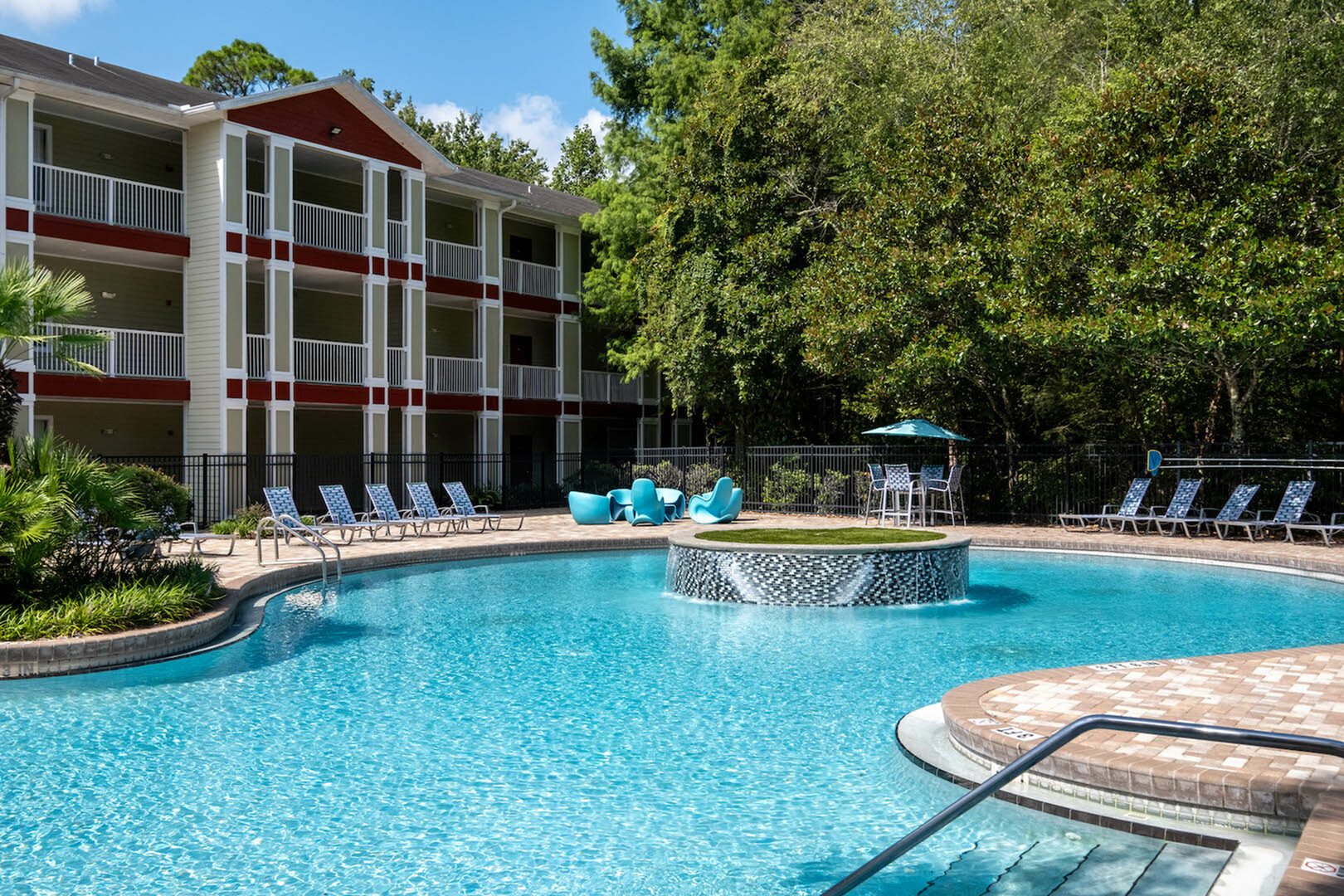 Inviting apartment complex featuring a sparkling outdoor pool with stylish lounge chairs and a serene garden backdrop.