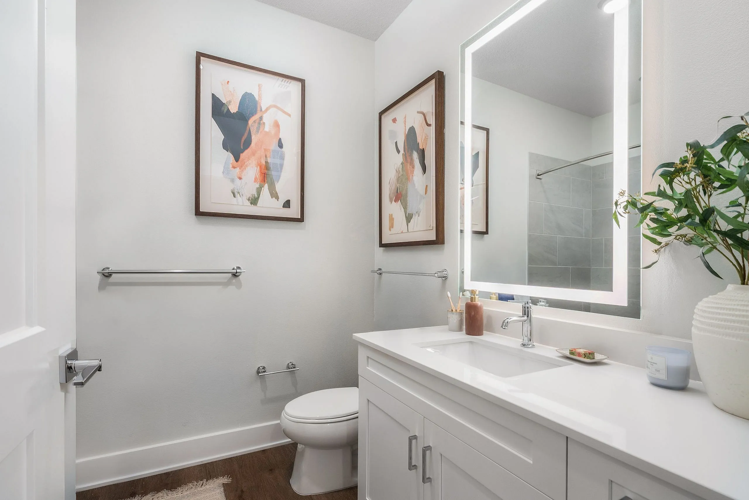 Bright, modern bathroom featuring a large illuminated mirror, sleek white vanity, and elegant wall art.