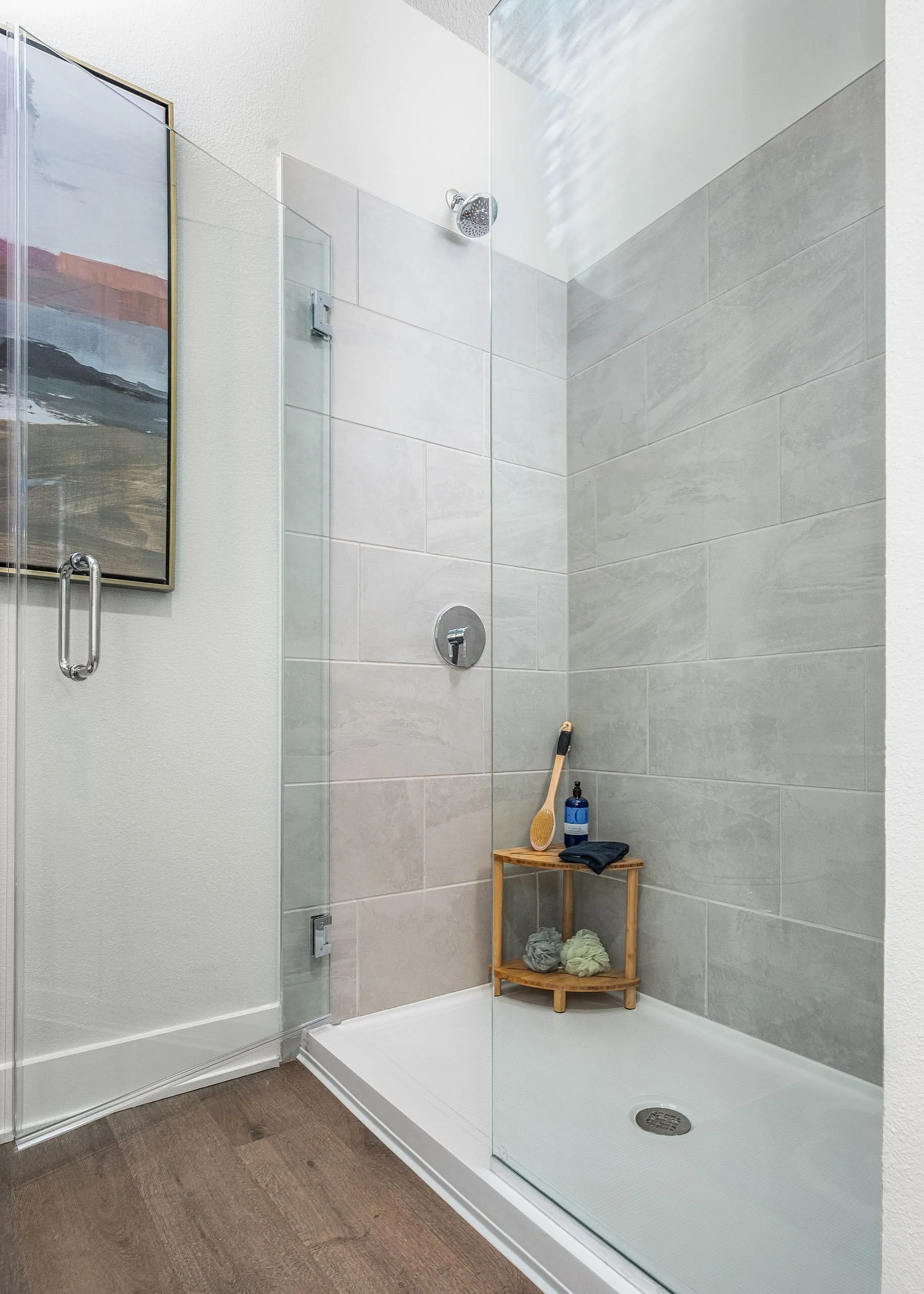 Elegant modern shower with sleek gray tiles, glass door, and stylish wooden shelf enhancing the bathroom's sophistication.
