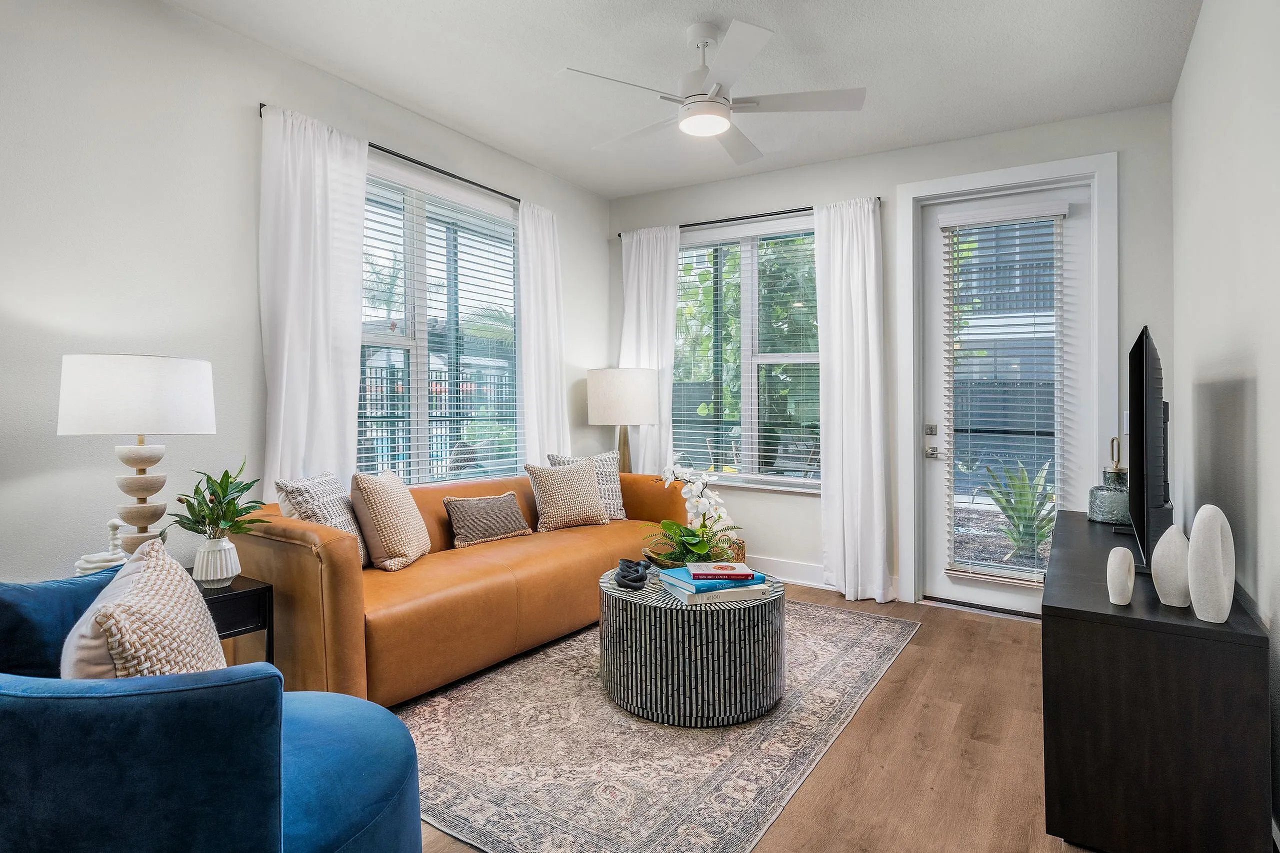 Bright, contemporary living room with elegant decor, featuring a comfortable leather sofa, stylish blue armchair, and large windows for plenty of natural light.