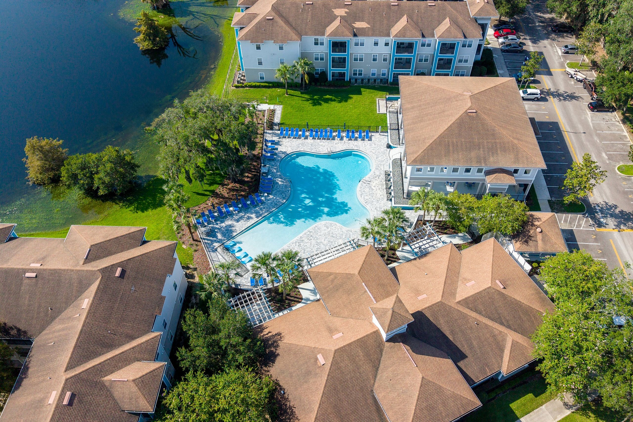 Aerial view of a luxurious apartment complex with a resort-style pool, lush greenery, and waterfront location.