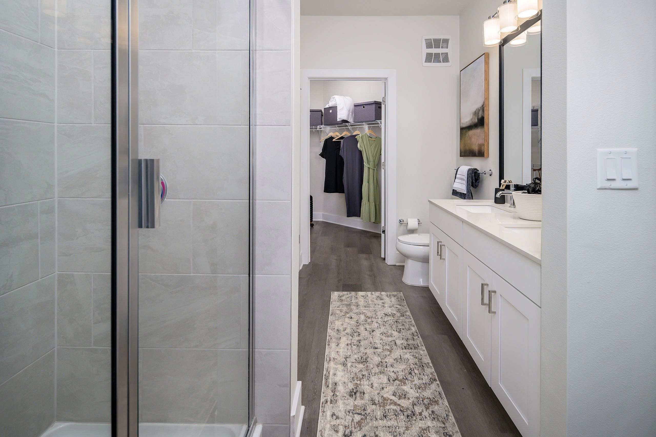 Elegant bathroom showcasing a modern glass shower, sleek white vanity with dual sinks, and walk-in closet for ample storage.