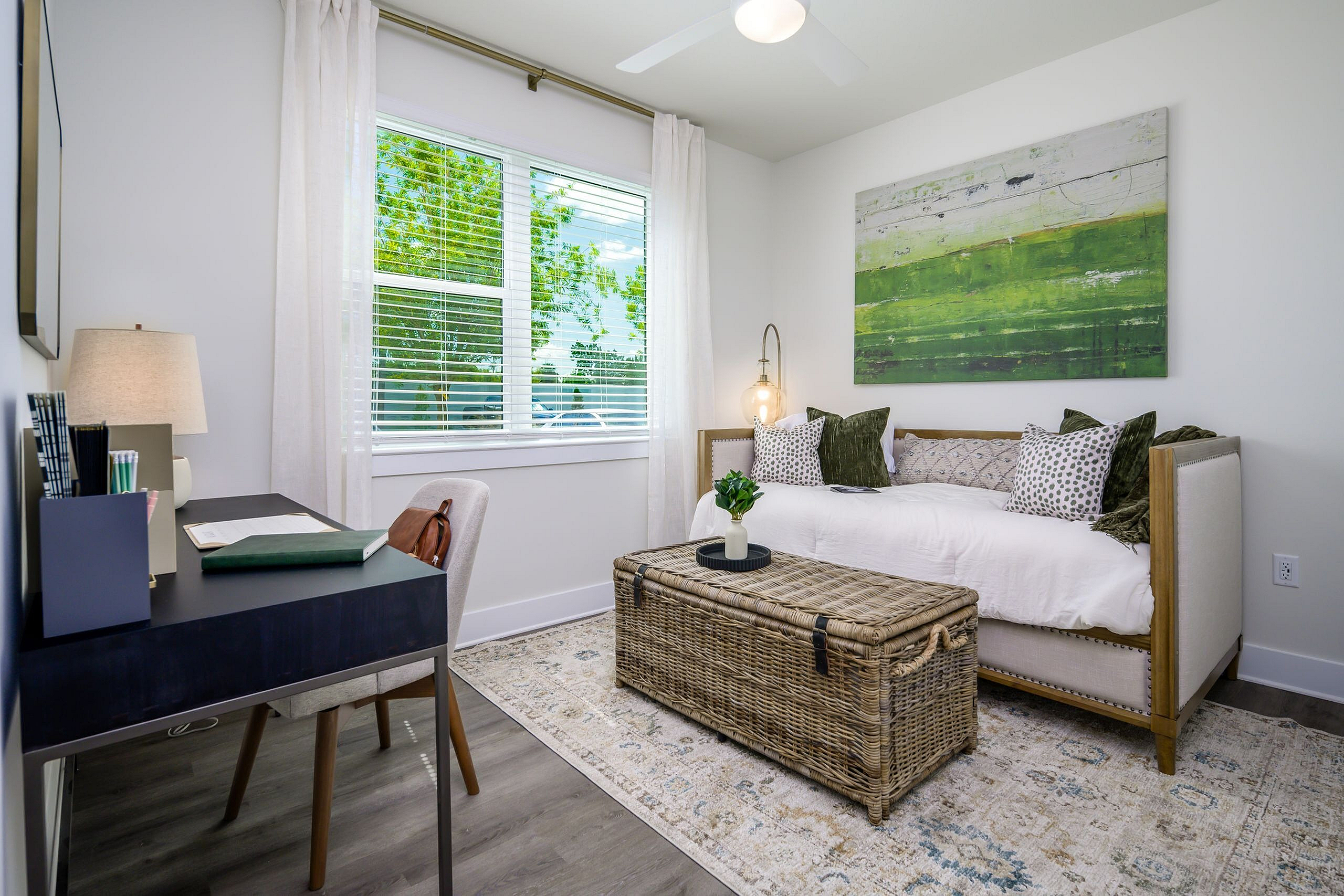 Bright and modern home office with a chic daybed, vibrant green artwork, and large window offering serene garden views.