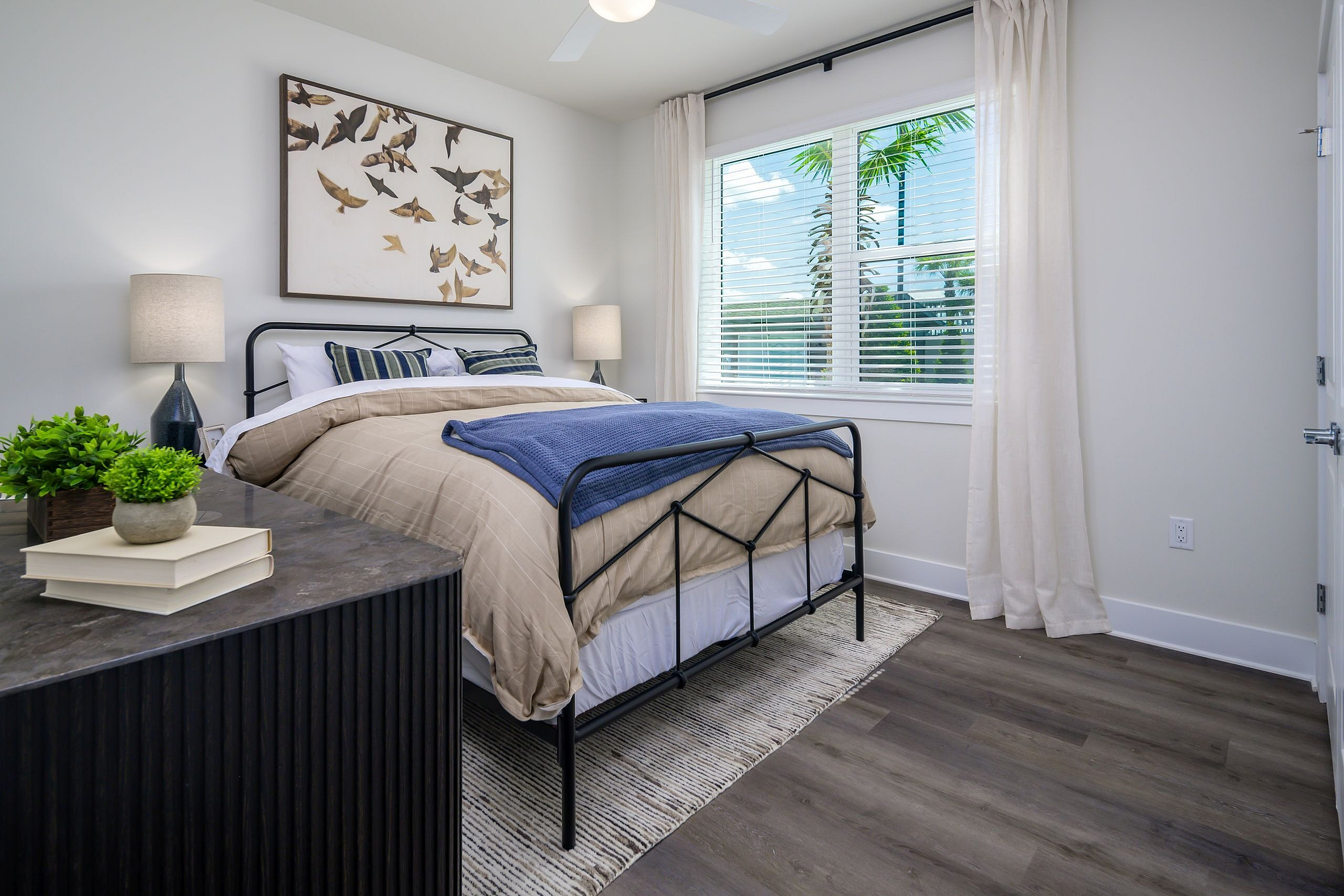 Charming bedroom with stylish decor and ample natural light, featuring a cozy bed, elegant artwork, and inviting greenery for a serene ambiance.