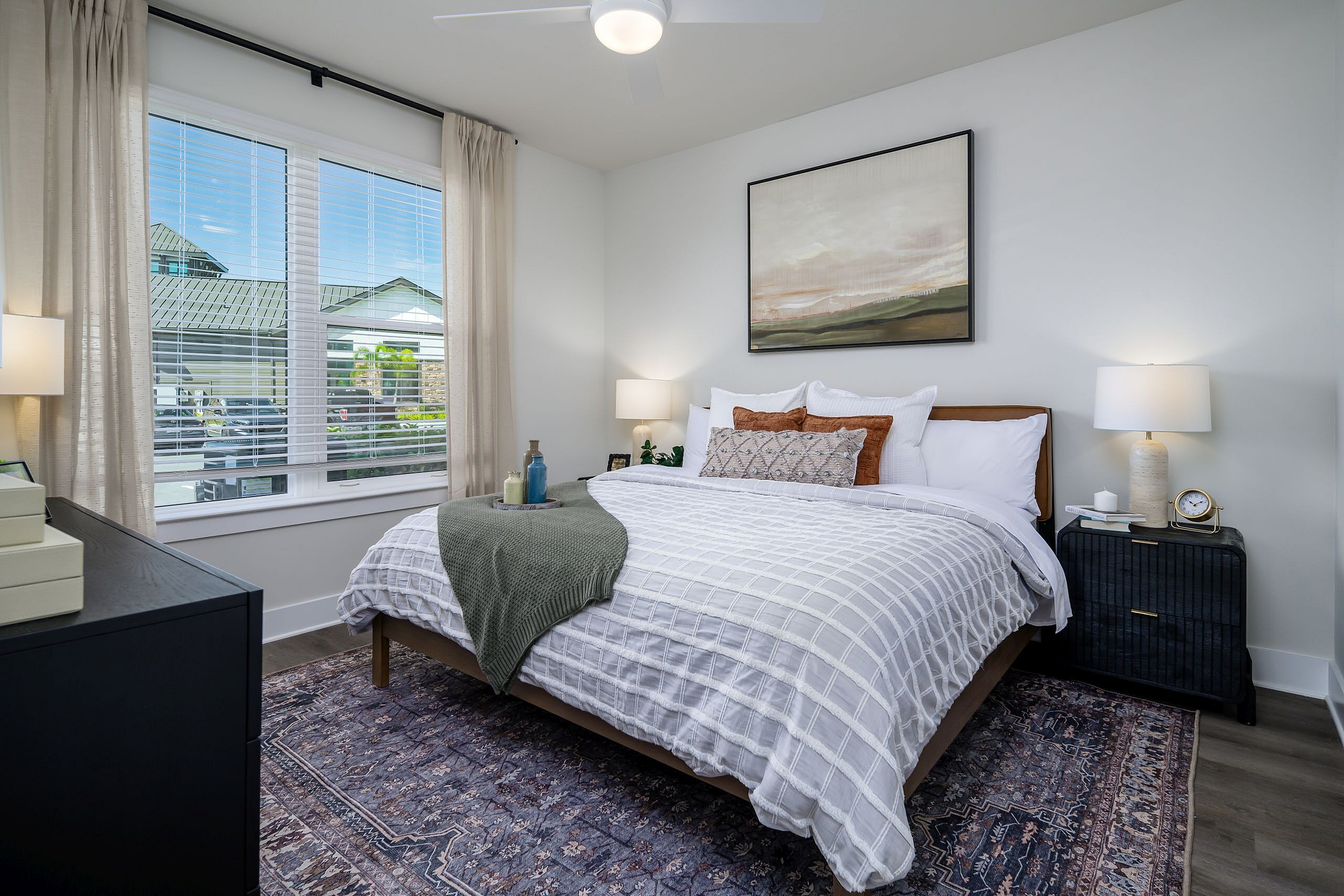 Inviting bedroom with elegant decor, large window with natural light, and a cozy bed with plush pillows and a chic throw blanket.