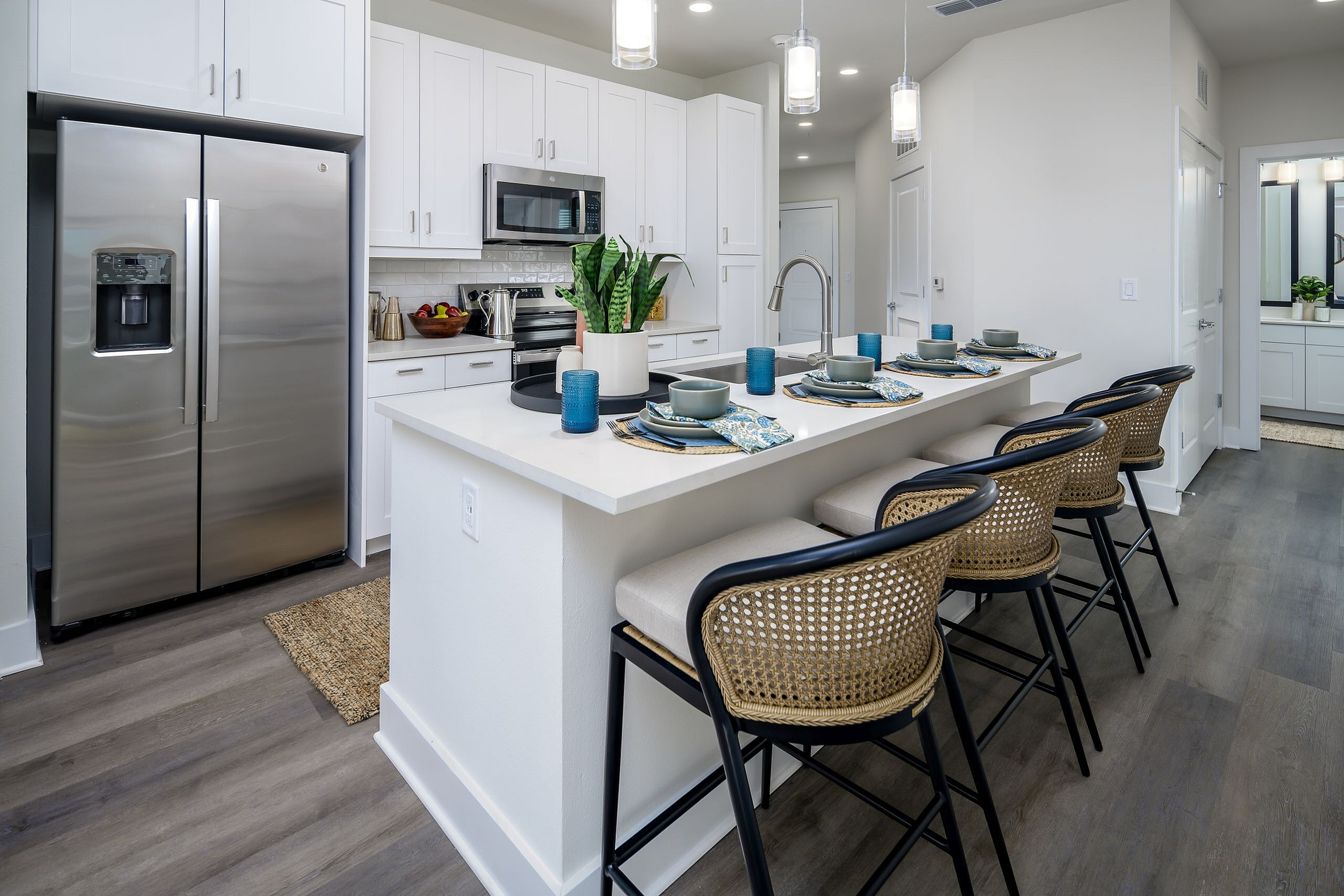 Modern kitchen featuring sleek stainless steel appliances, elegant white cabinetry, and a chic breakfast bar with stylish woven barstools.