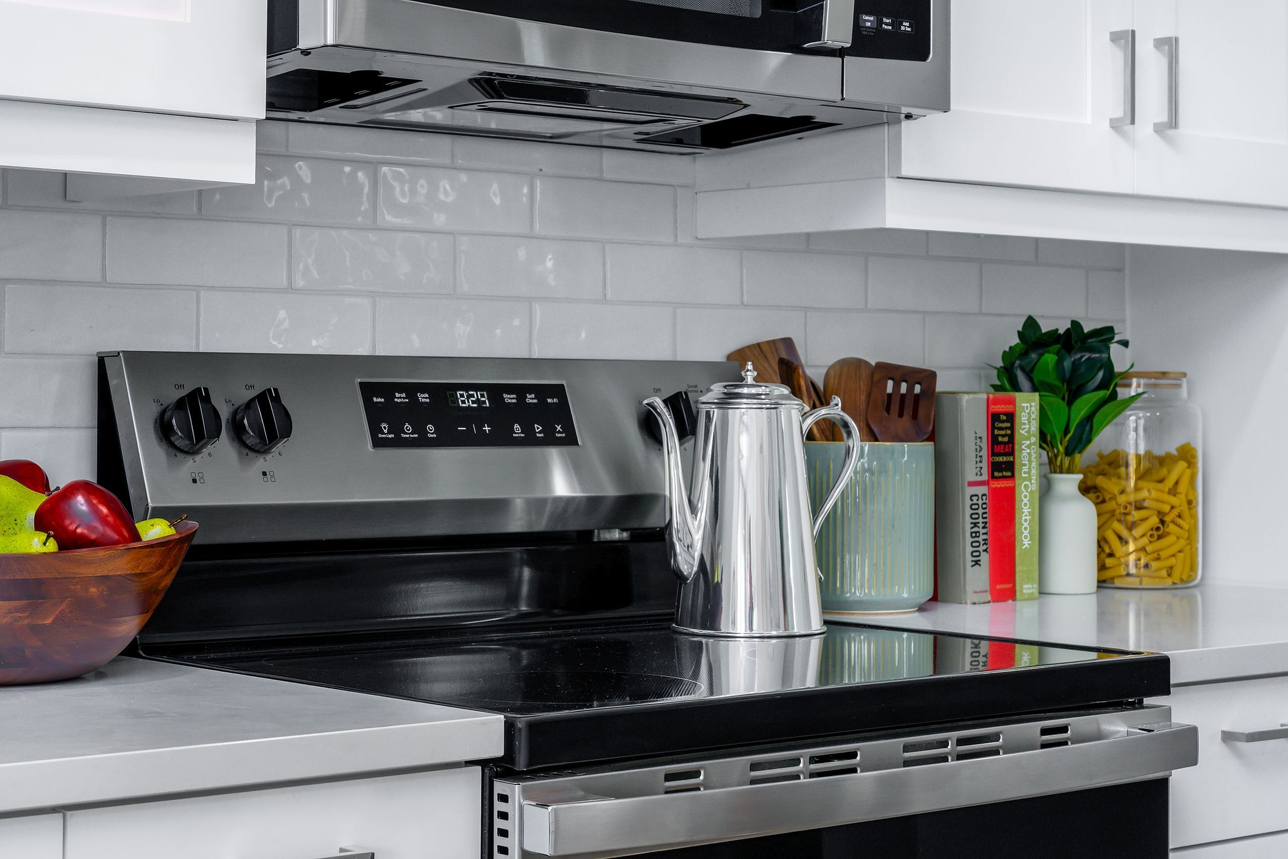 Sleek modern kitchen with stainless steel oven and chic backsplash, complemented by decorative cookbooks and a vibrant fruit bowl.