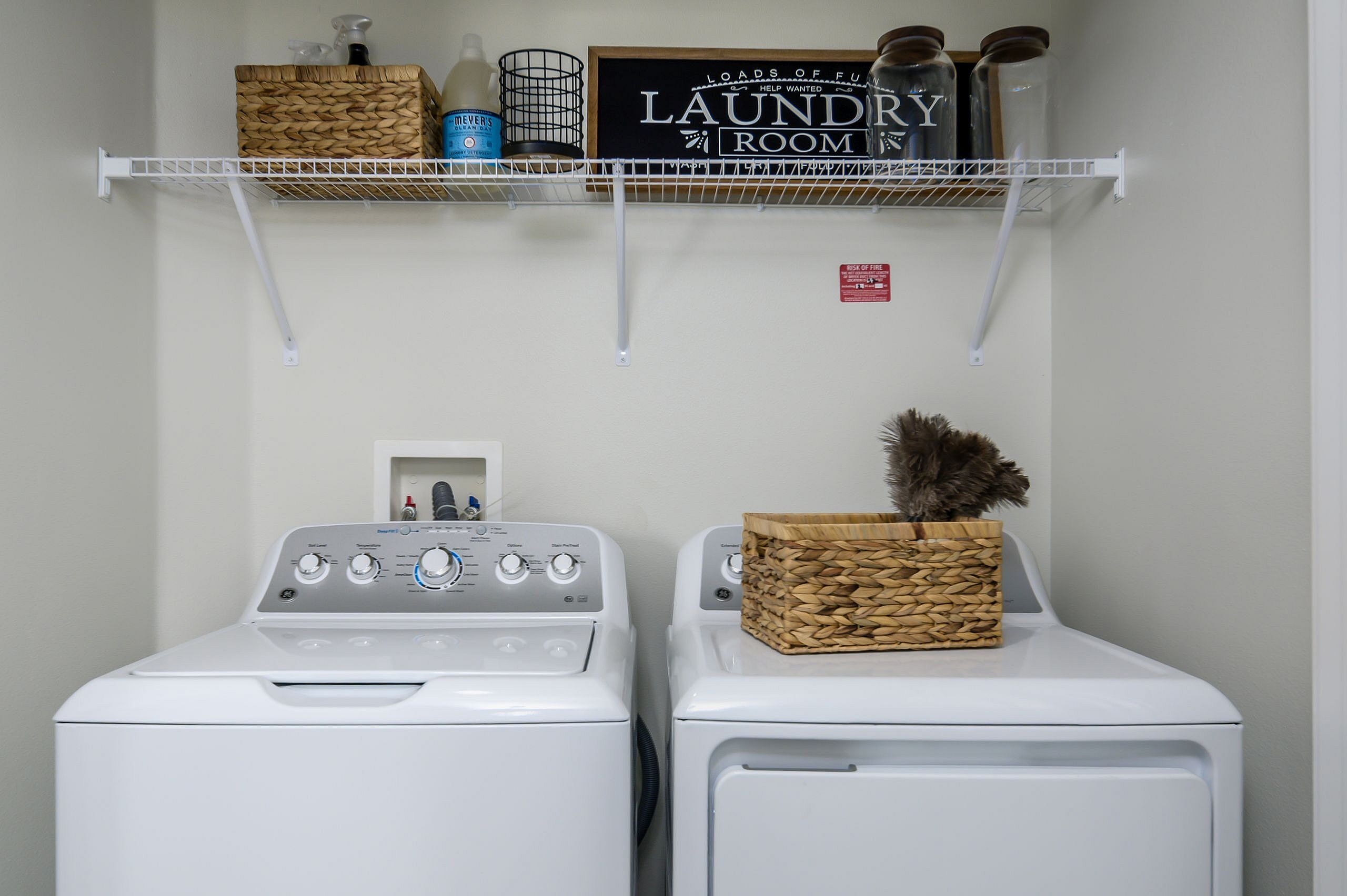 Modern laundry room featuring sleek white washer and dryer, wicker storage baskets, and stylish shelving.