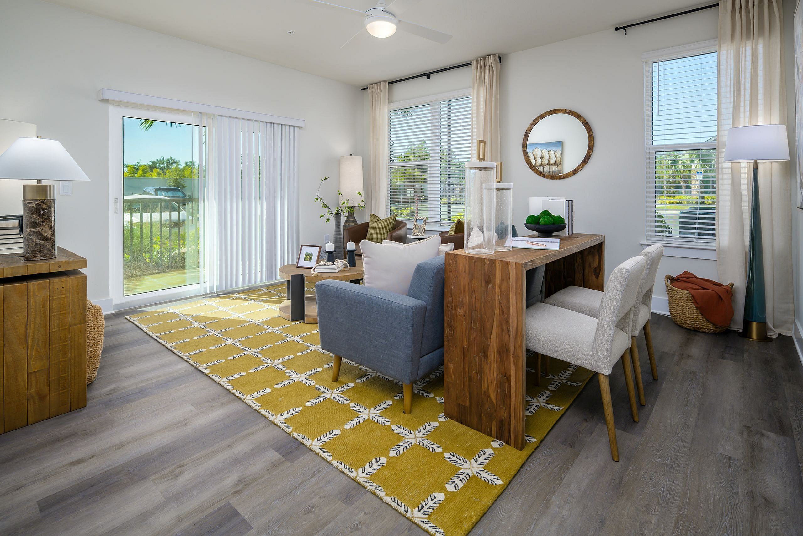 Contemporary living room with abundant natural light, featuring elegant wood furniture, vibrant yellow rug, and sliding glass doors leading to a serene outdoor view.