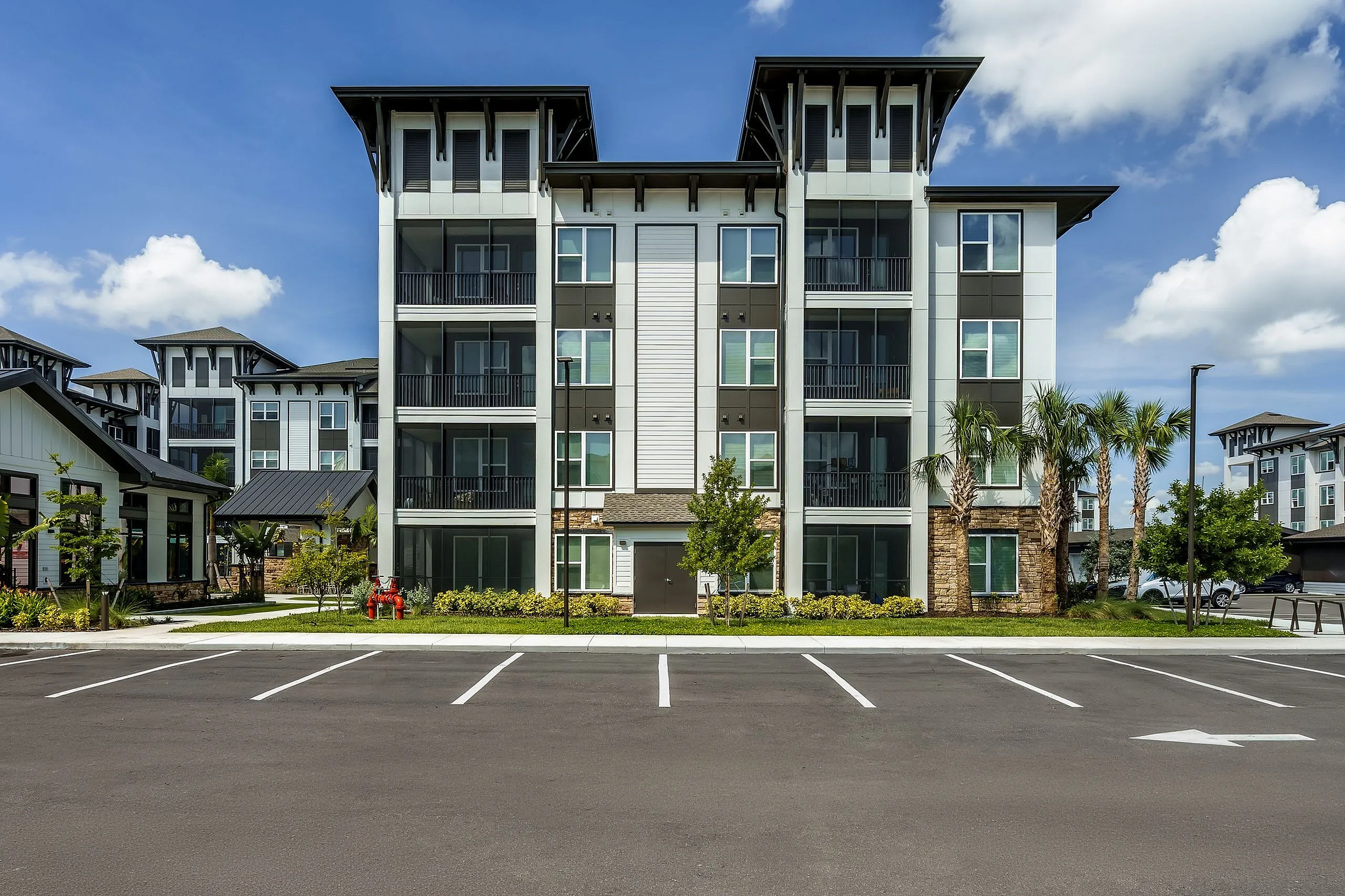 Modern apartment complex with sleek architecture, featuring spacious balconies and lush landscaping under a bright blue sky.
