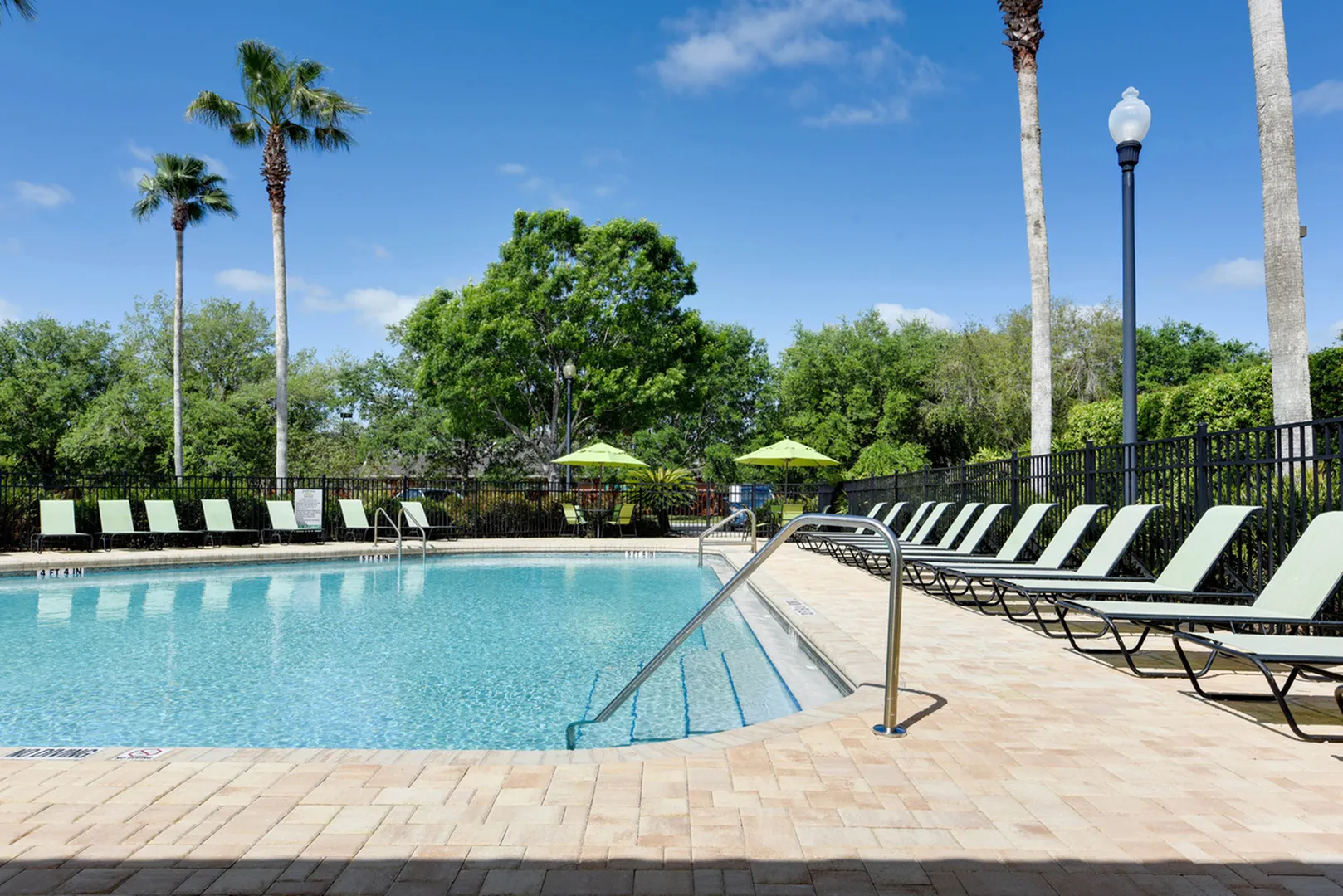Beautiful resort style pool lined with lounge chairs.  Trees in the distance.