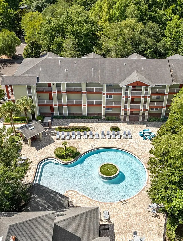 Aerial view of a modern apartment complex with a stunning resort-style pool, surrounded by lush greenery and outdoor seating for relaxation.