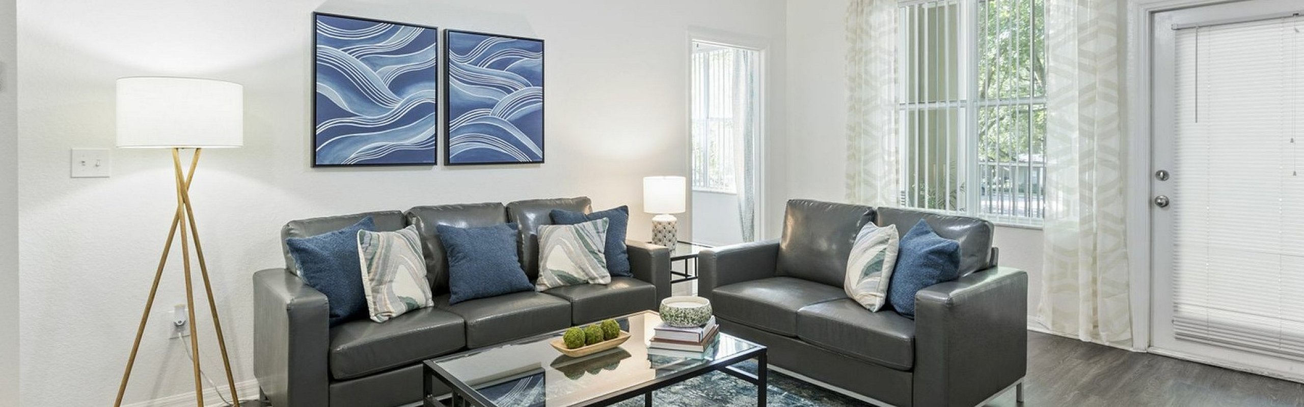 Modern living room with sleek gray sofas, stylish blue and white decor, and abundant natural light.