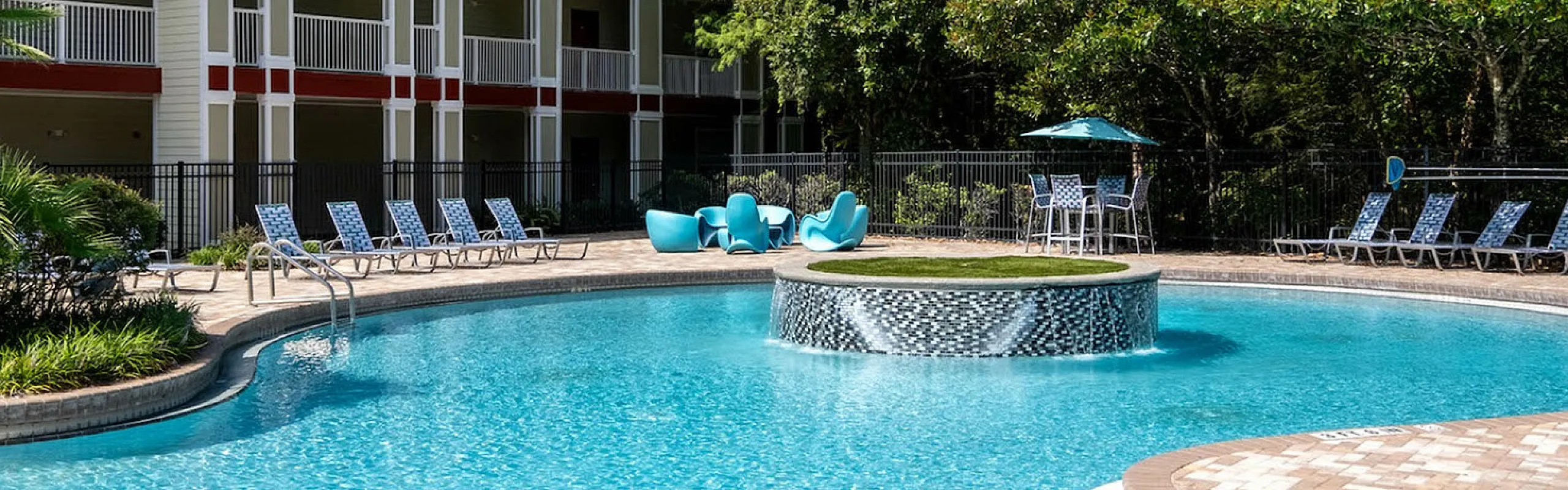 Inviting apartment community with a sparkling resort-style pool, surrounded by lush greenery and modern outdoor seating.