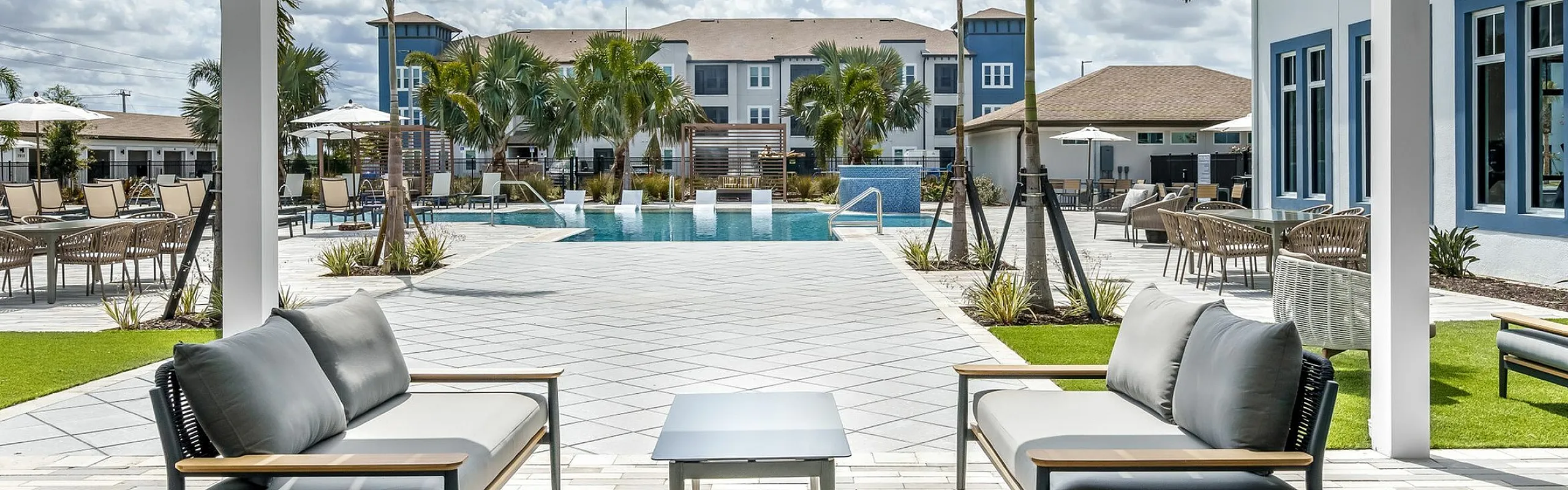 Luxurious outdoor patio with stylish seating and a sparkling pool, surrounded by palm trees under a bright blue sky.