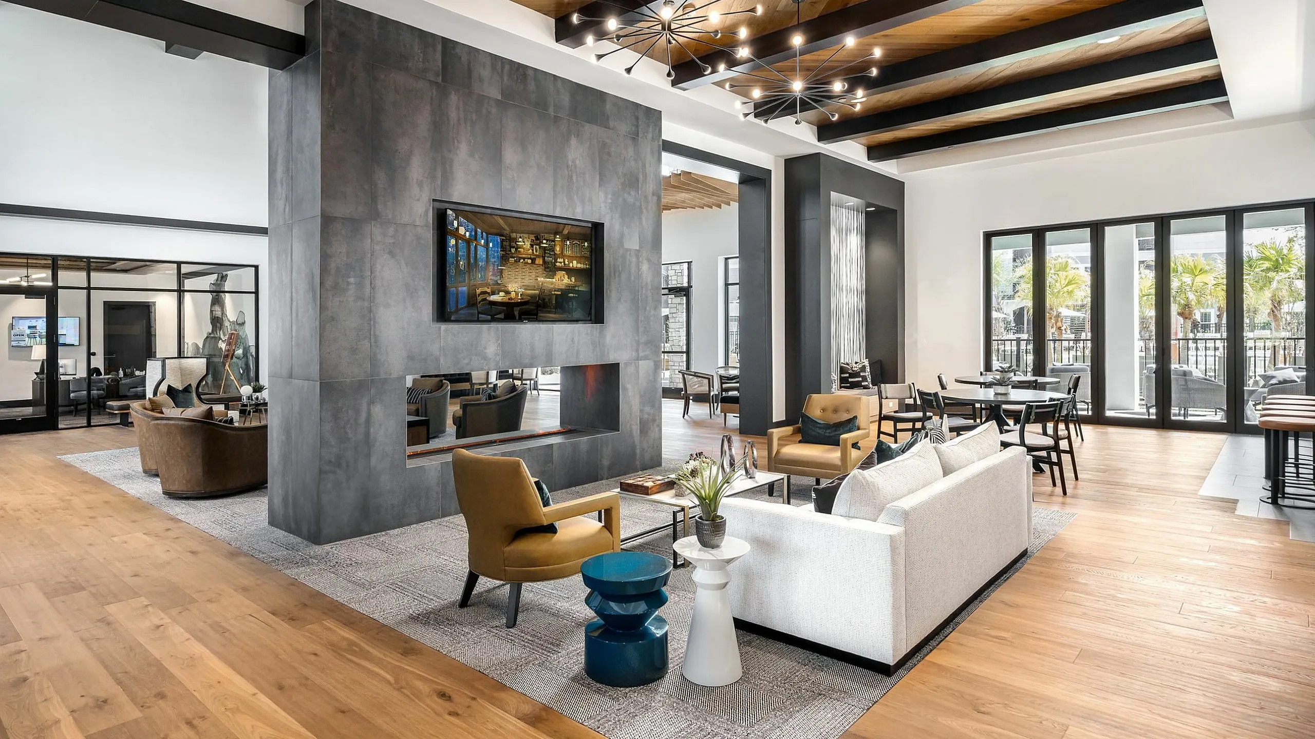 Luxurious open-concept living area featuring modern furnishings, elegant lighting, and expansive hardwood floors with large windows overlooking tropical foliage.