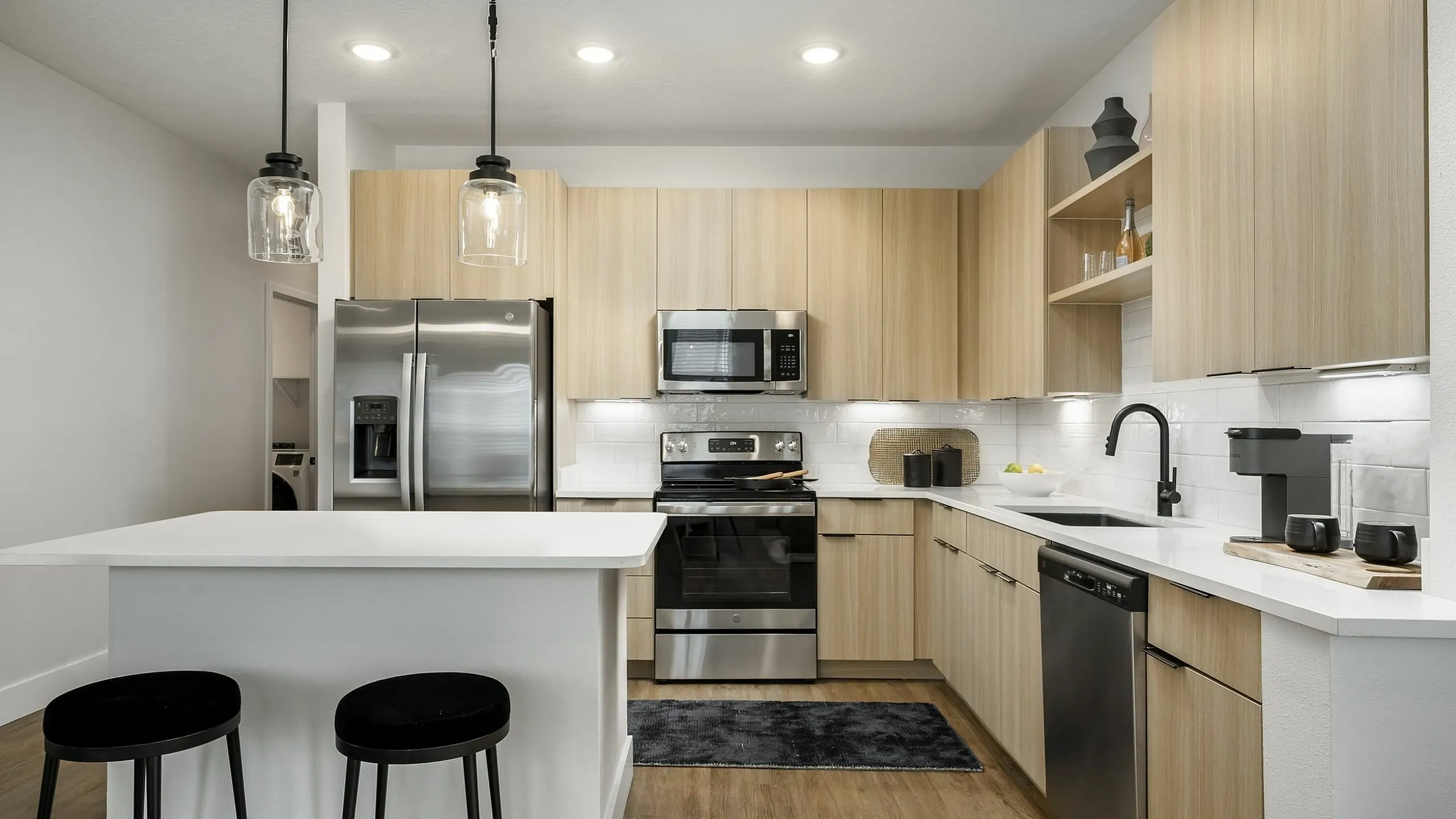 Modern kitchen with sleek stainless steel appliances, warm wooden cabinetry, and elegant pendant lighting over a spacious island with bar stools.