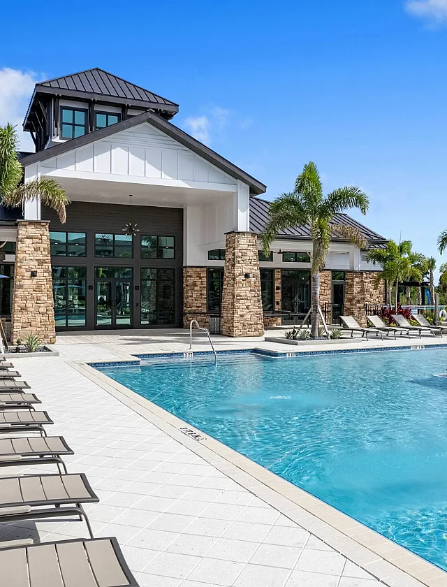 Luxurious resort-style pool area with sun loungers and tropical landscaping, featuring a modern clubhouse under a clear blue sky.